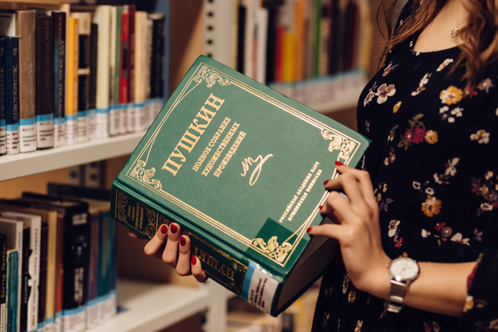 Woman opening a book in front of a bookshelf