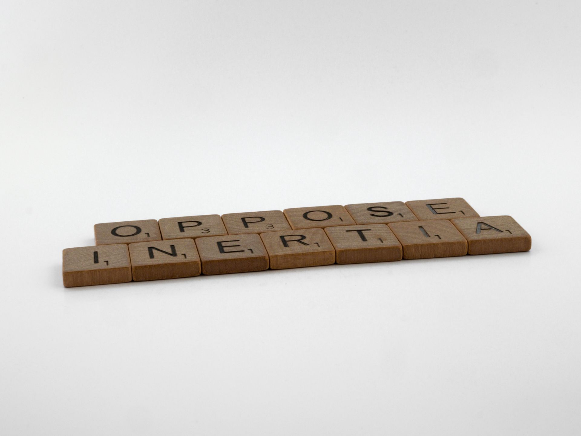 Wooden Scrabble tiles spelling Oppose Inertia on white
