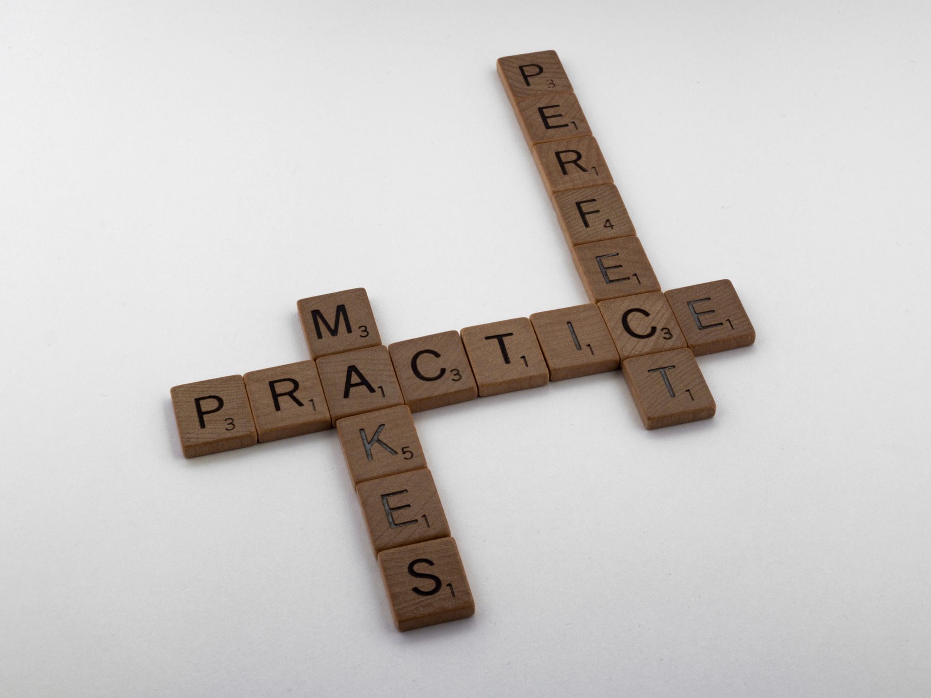 Wooden Scrabble tiles spelling Practice Makes Perfect