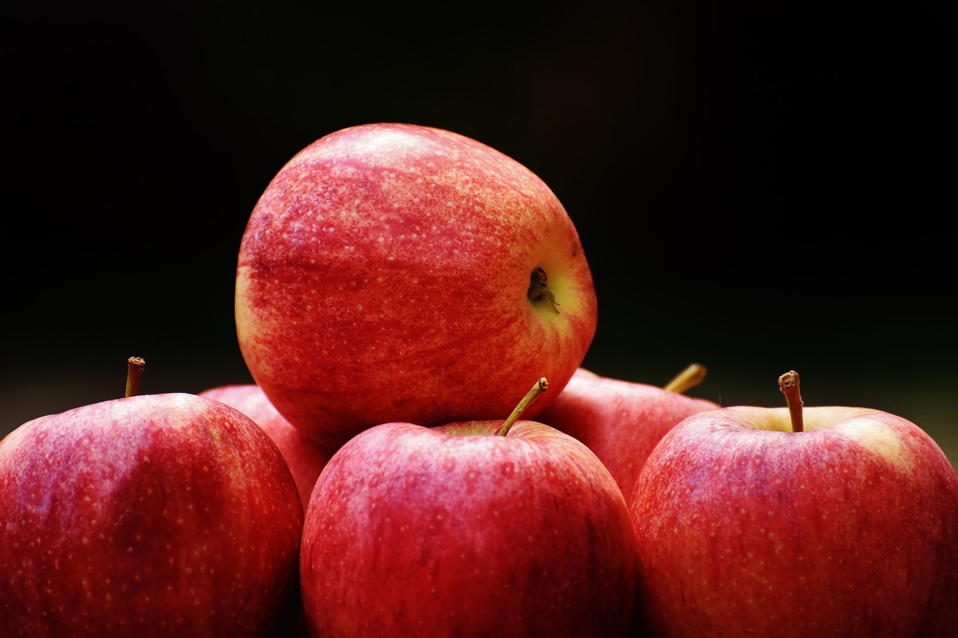 Cluster of ripe red apples stacked against a dark backdrop