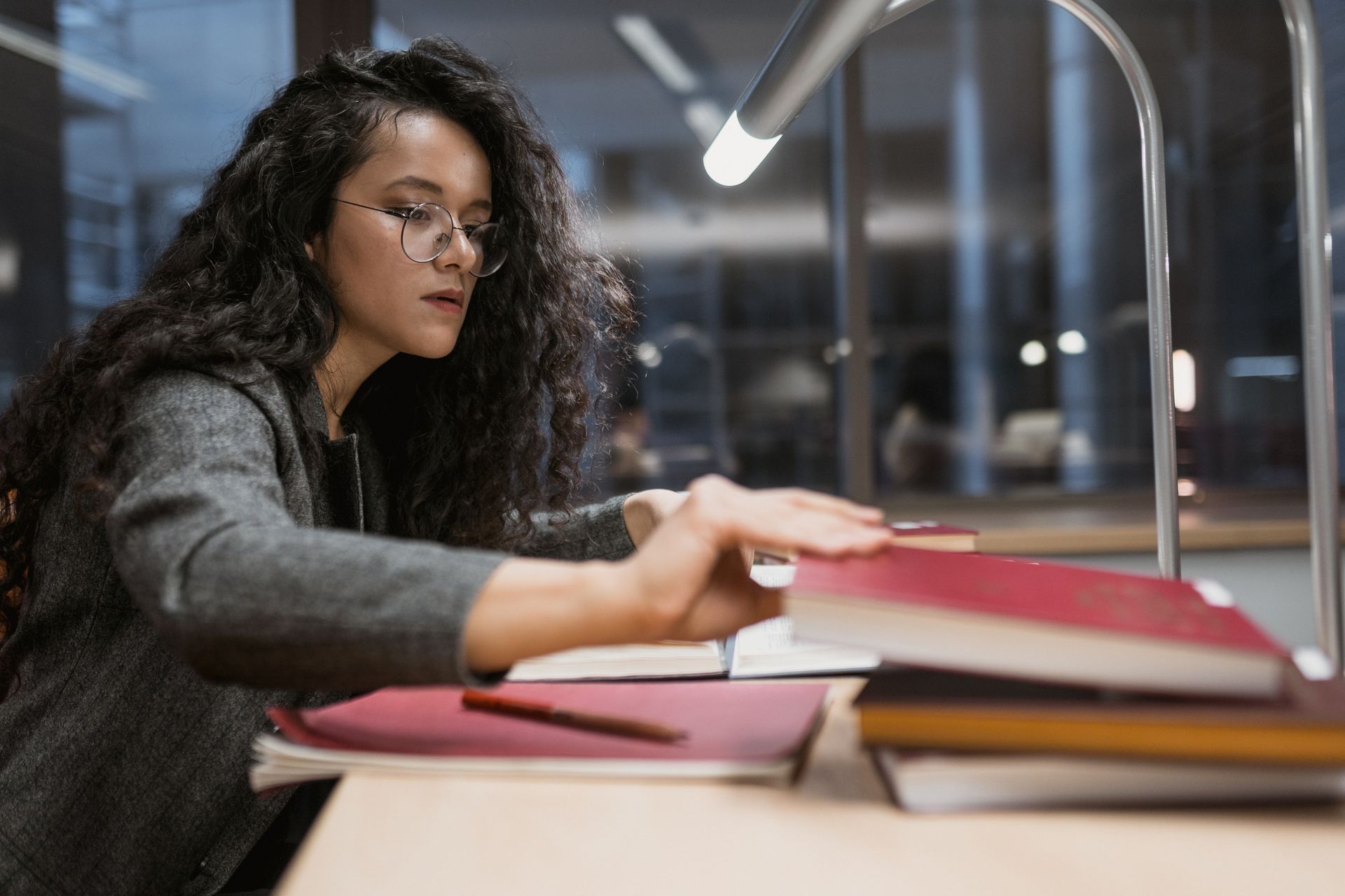 Woman with glasses studying at a desk under a lamp at night