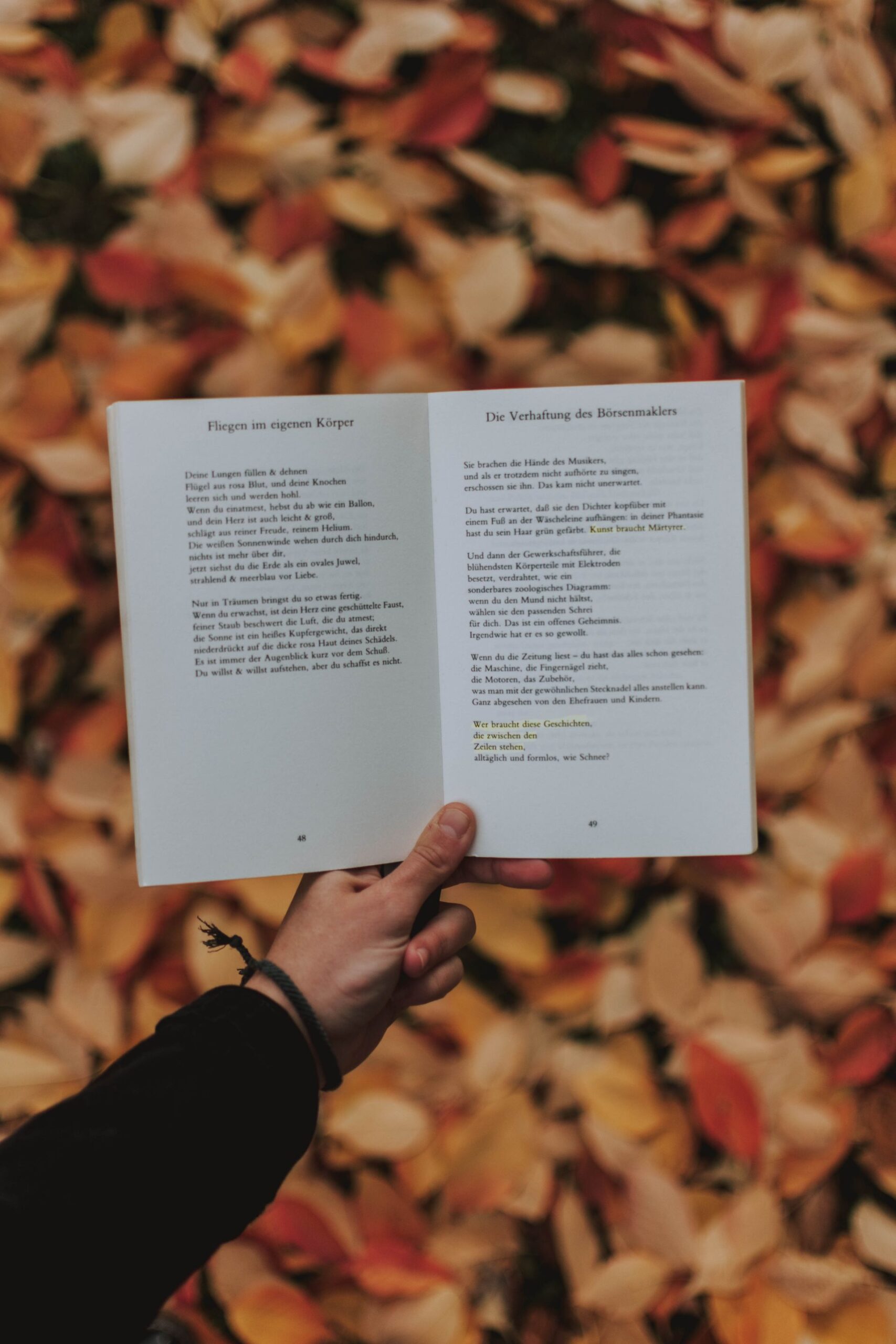 Person holding an open poetry book among autumn leaves