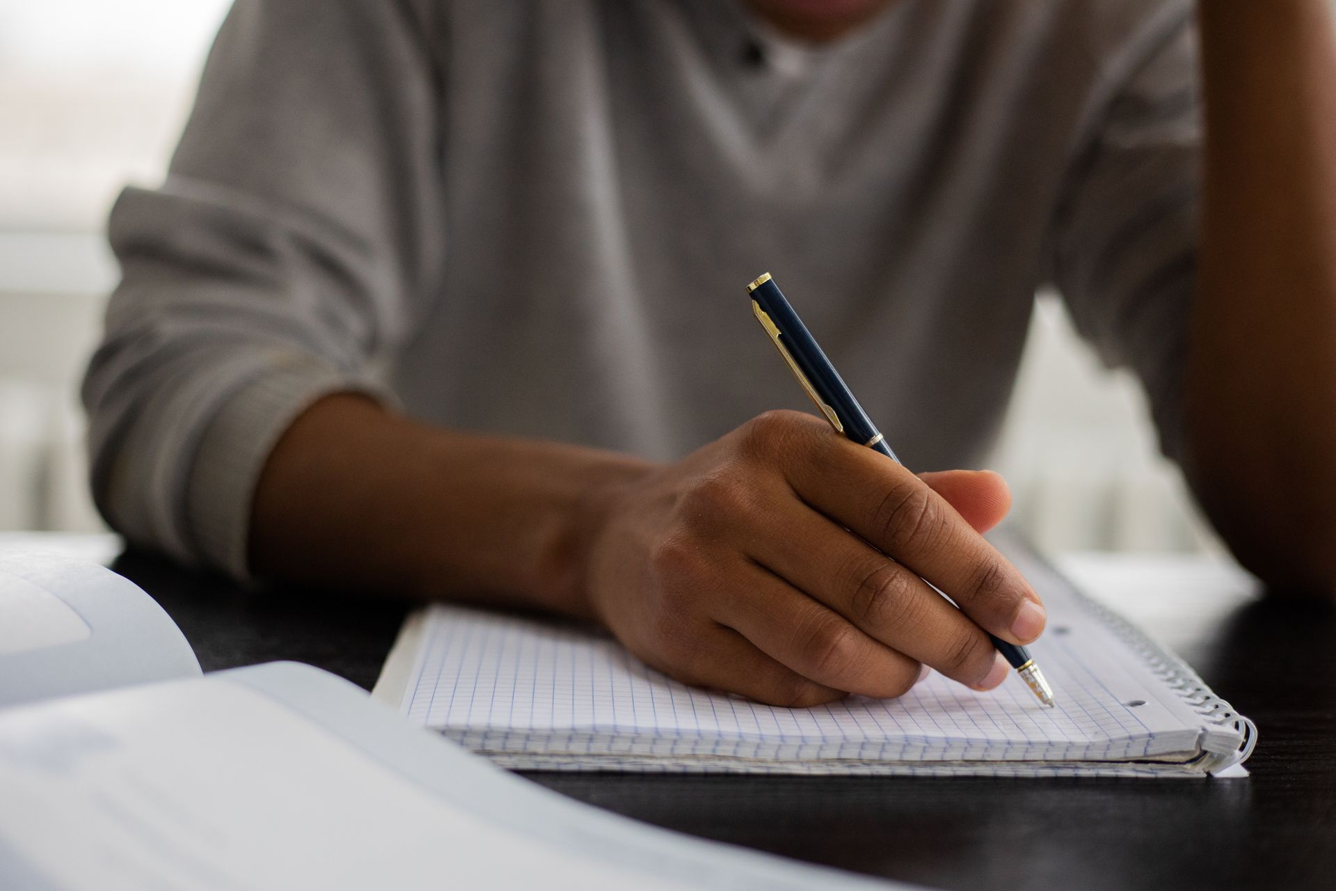 Student taking notes in a workbook with a textbook nearby