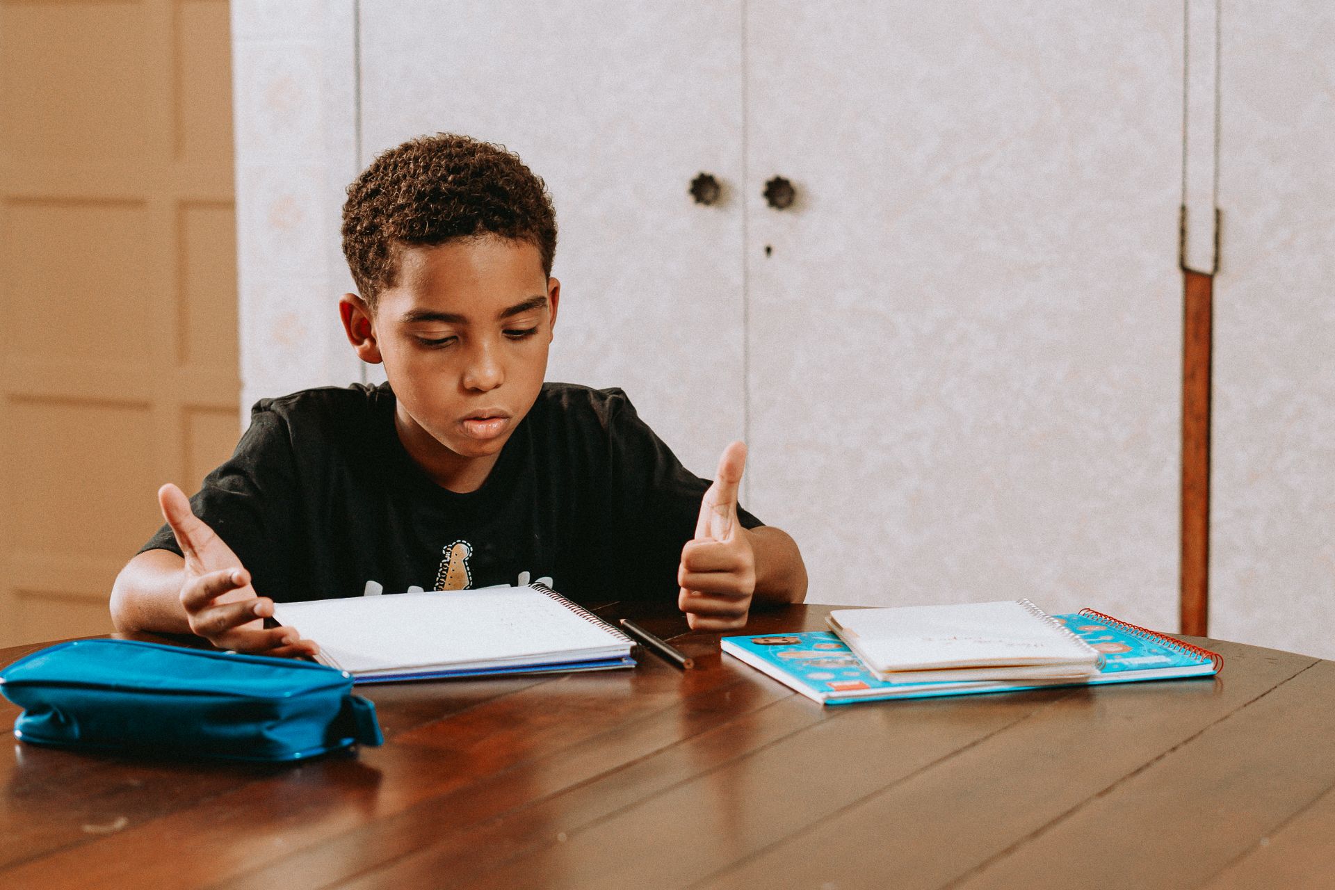 Boy doing homework at a wooden table with notebooks