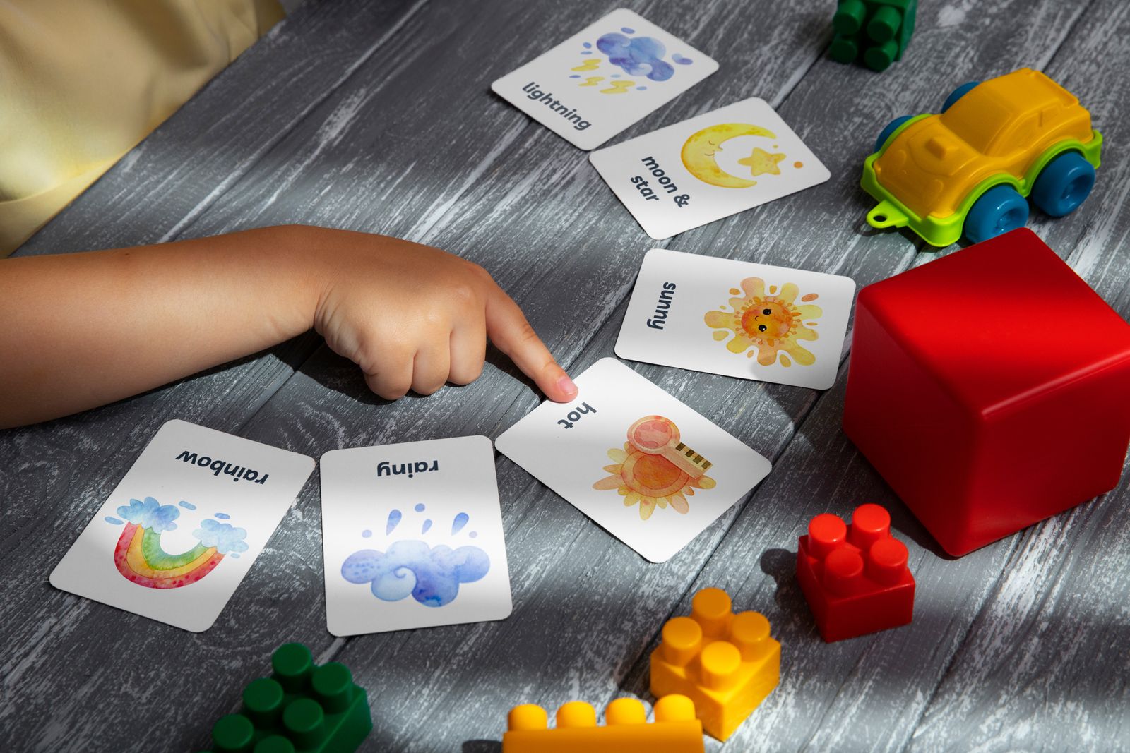 Child pointing at a learning card on a table with toys