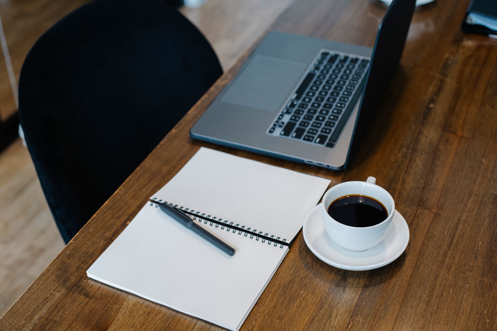 High angle of opened laptop and spiral notebook with blank pages on a wooden table with cup of coffee and pen