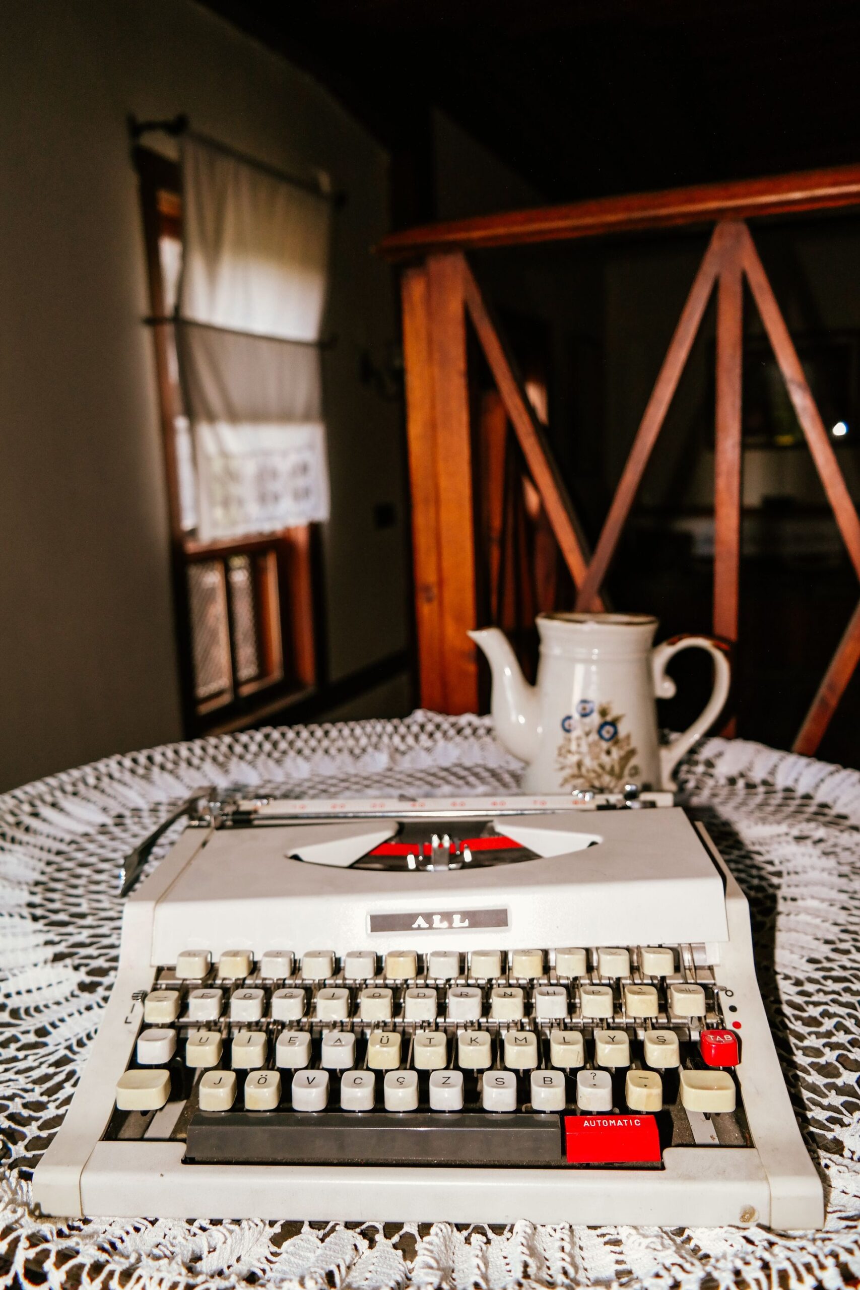 A retro still life featuring a typewriter and teapot on a lace-covered table indoors.
