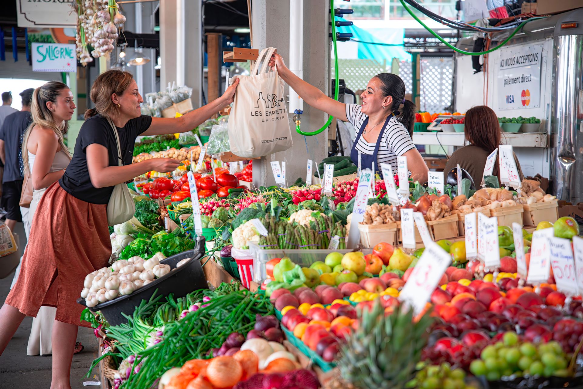 Women shopping at a colorful outdoor market stall filled with fresh fruits and vegetables