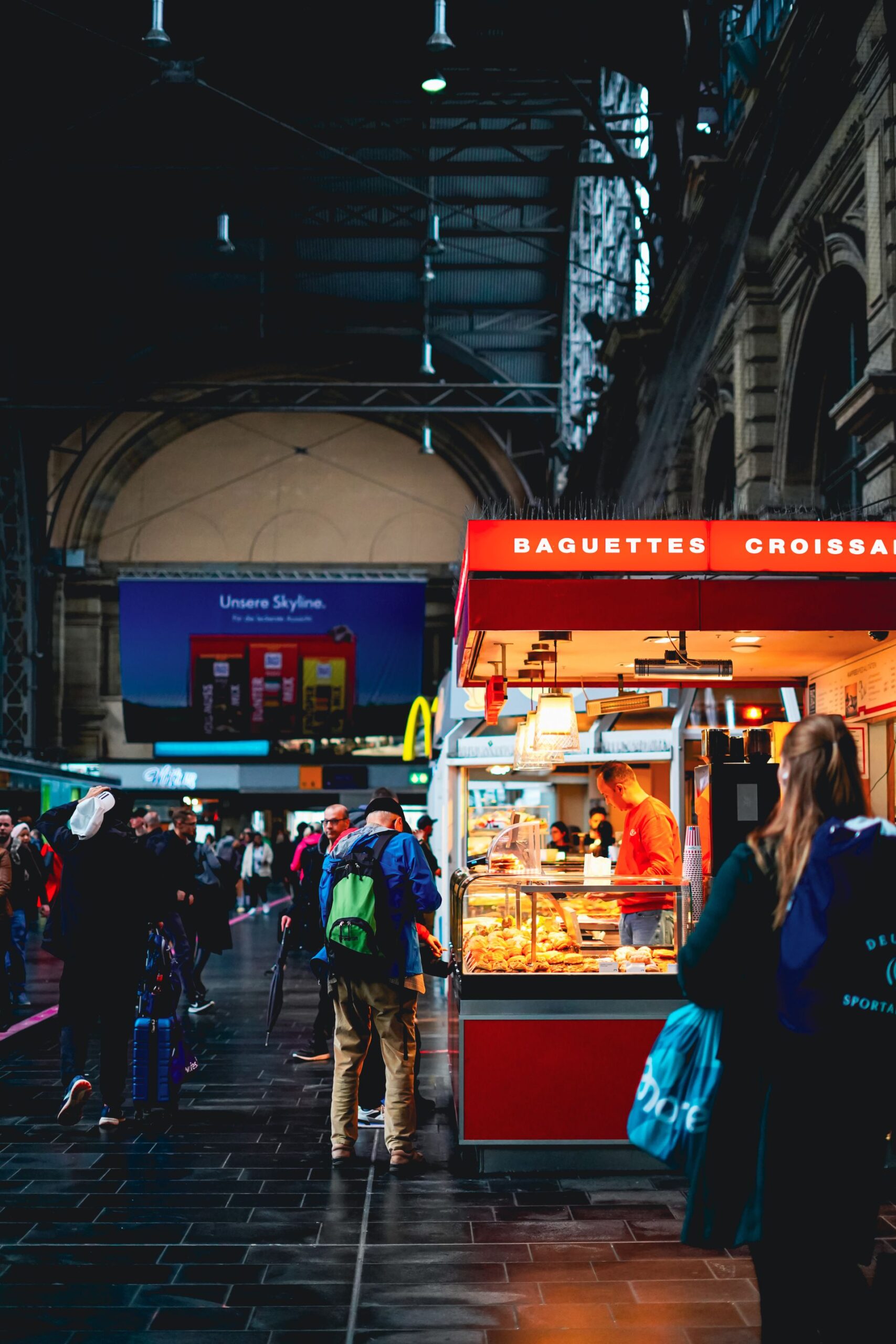 Frankfurt train station with a bakery stand selling baguettes and croissants, bustling with people