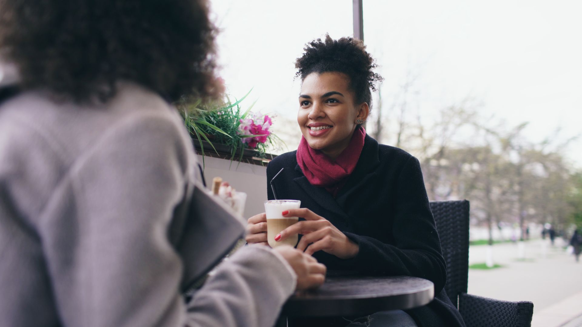 Two women enjoying a warm coffee chat at an outdoor cafe, relaxed and happy