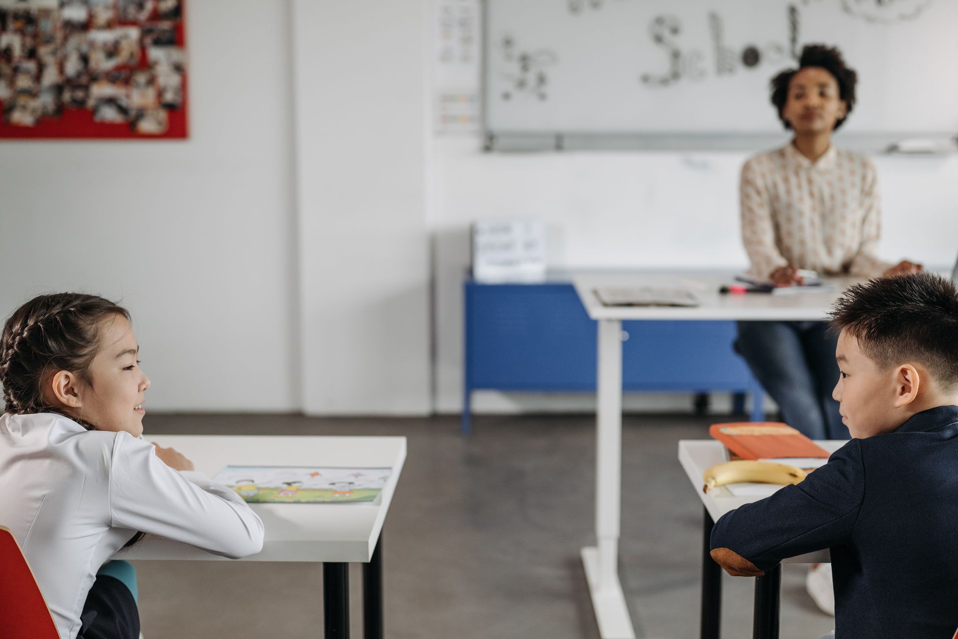 Two students in a classroom with their teacher in the background