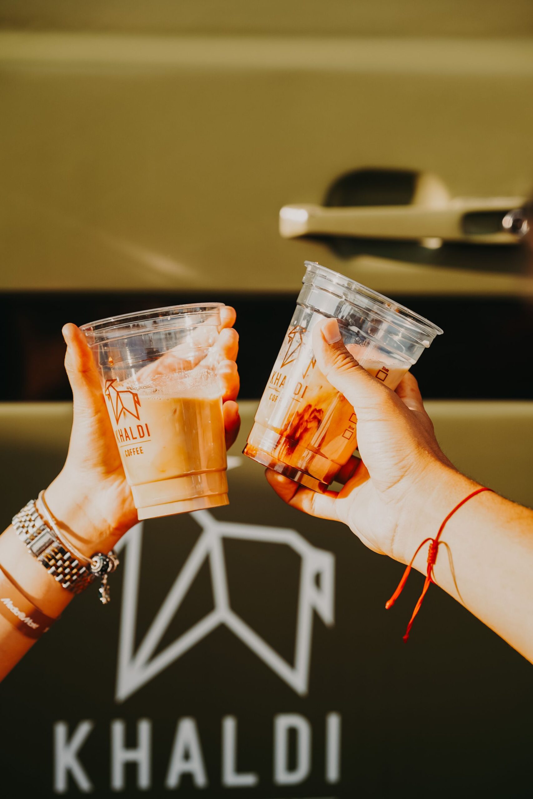 Two women holding iced coffee cups in a cheers gesture