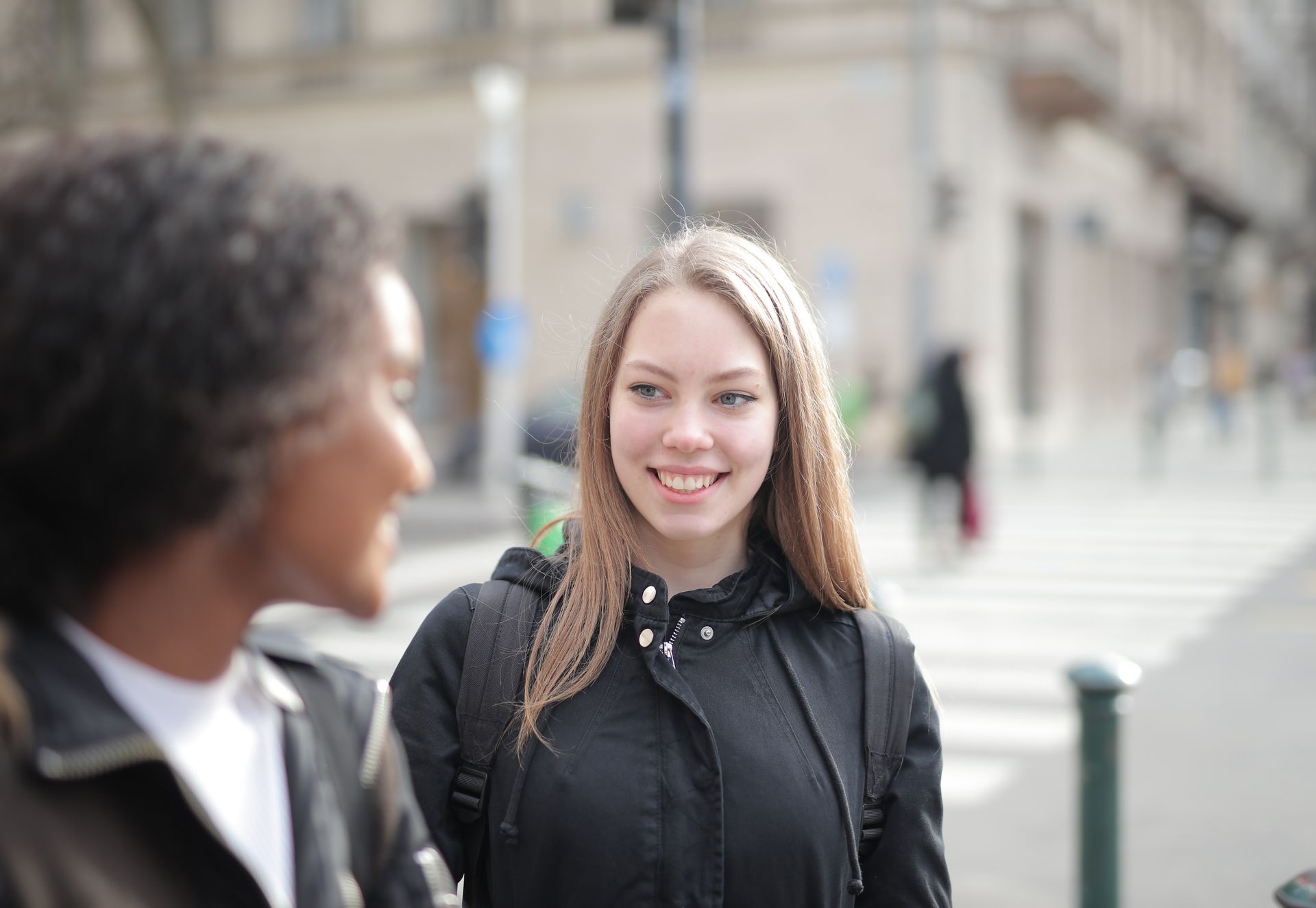 Two young women smiling and talking on a city street