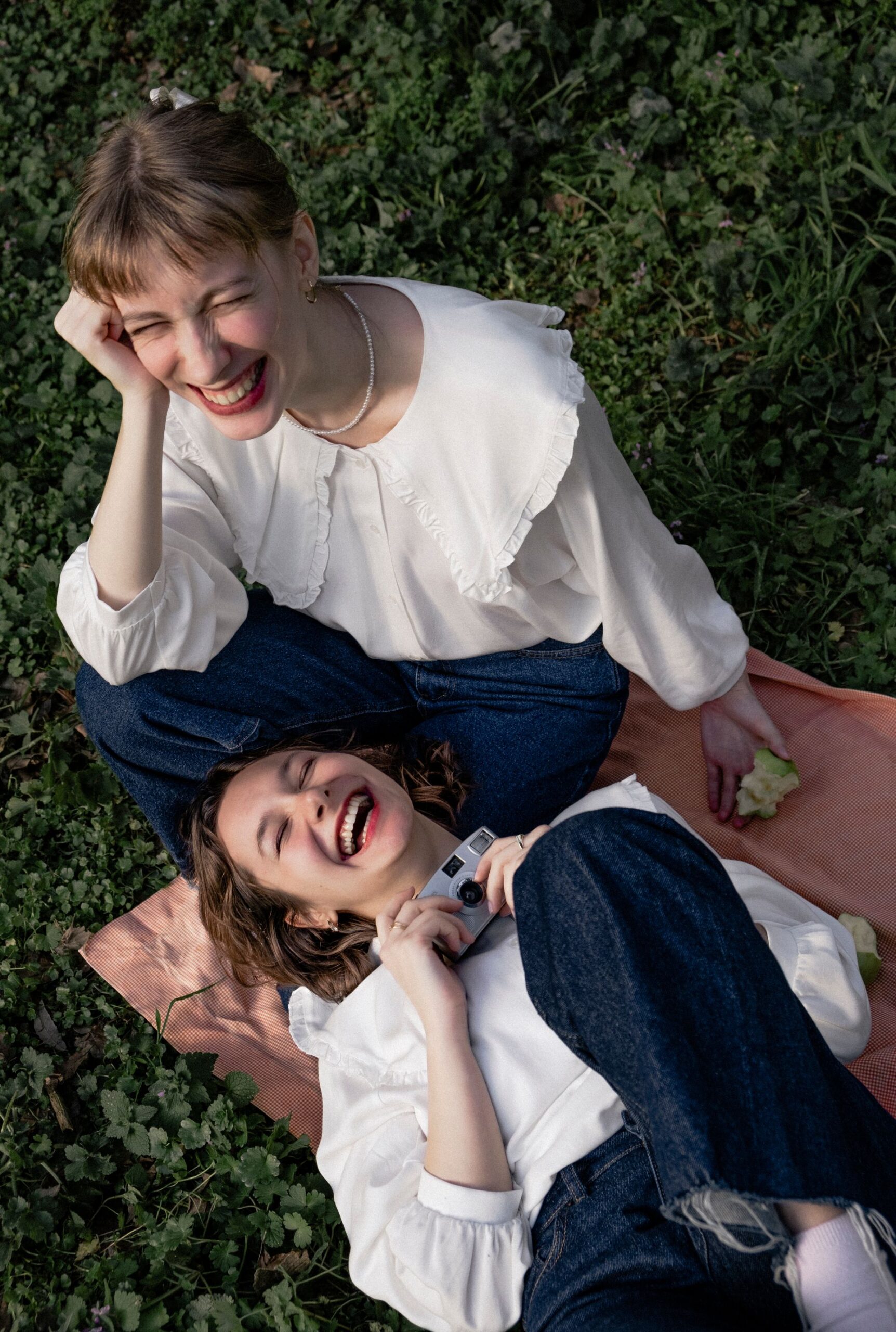 Two women laughing while lying on a picnic blanket outdoors