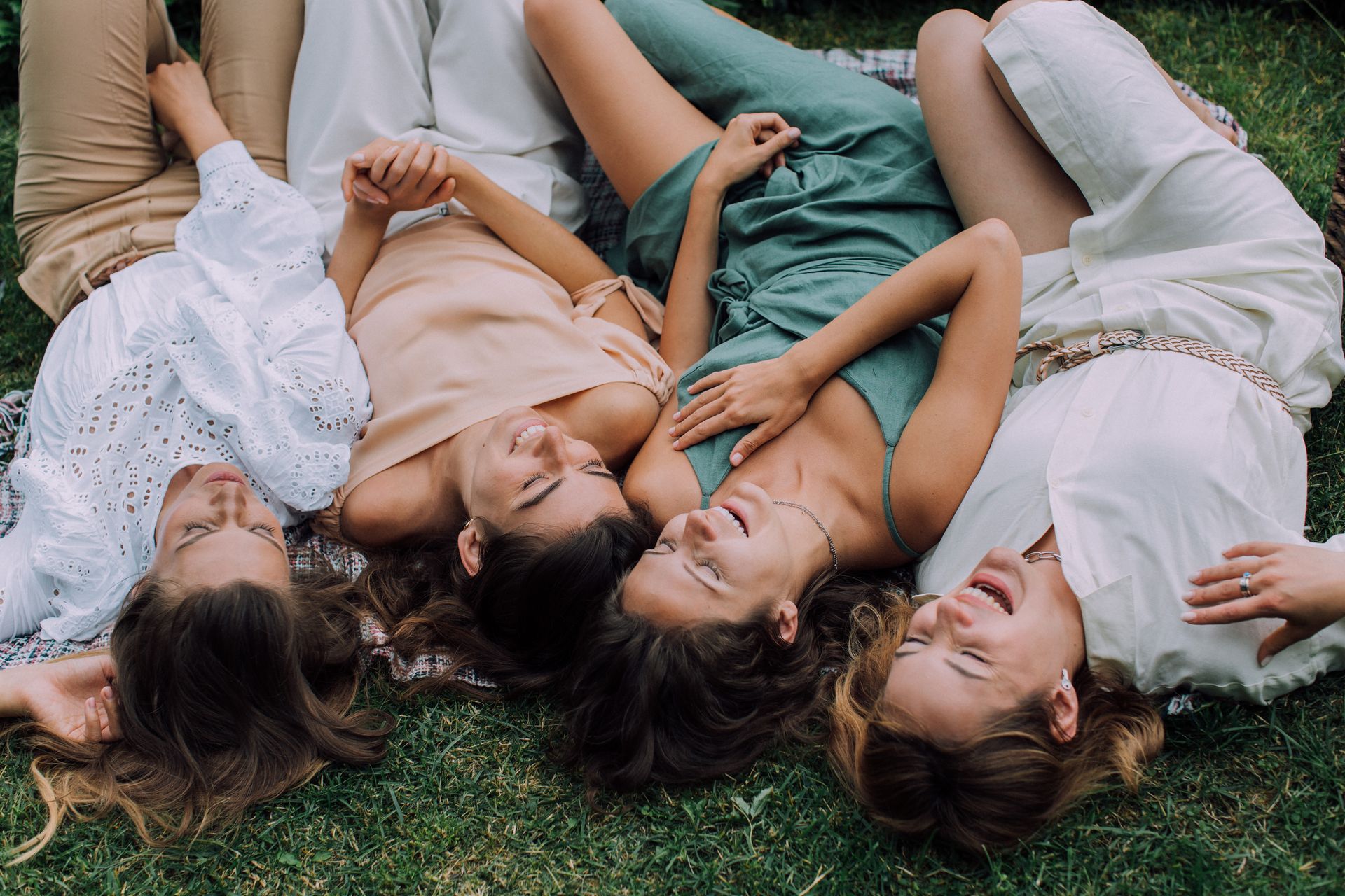 Four women laughing together lying on the grass