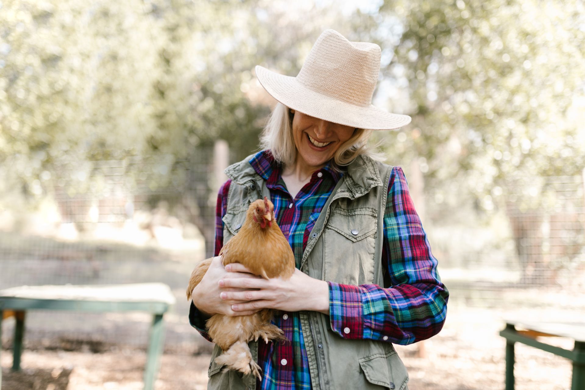 Smiling woman holding a brown hen on a farm