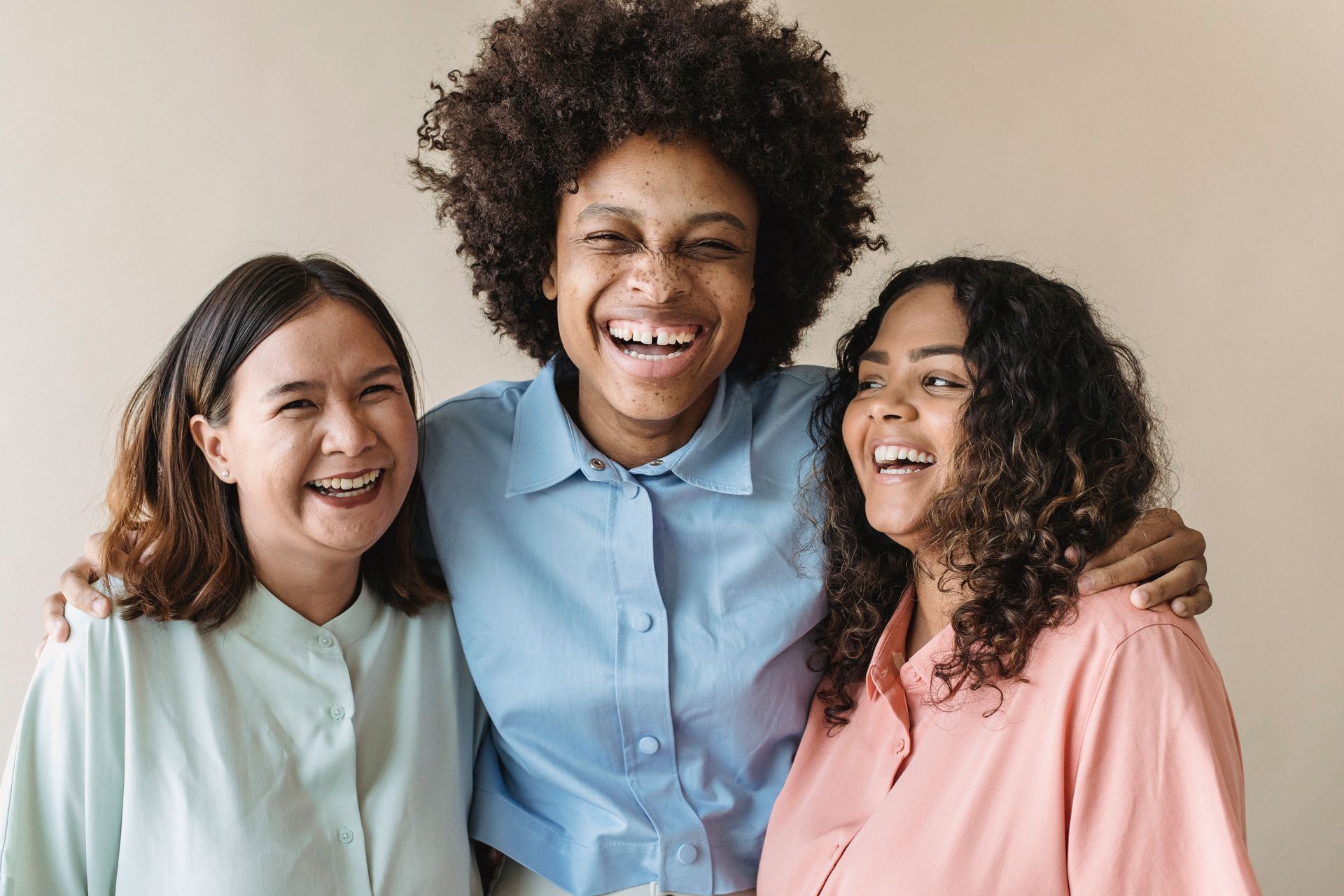 Three women of diverse backgrounds sharing a joyful moment, showcasing happiness and unity.