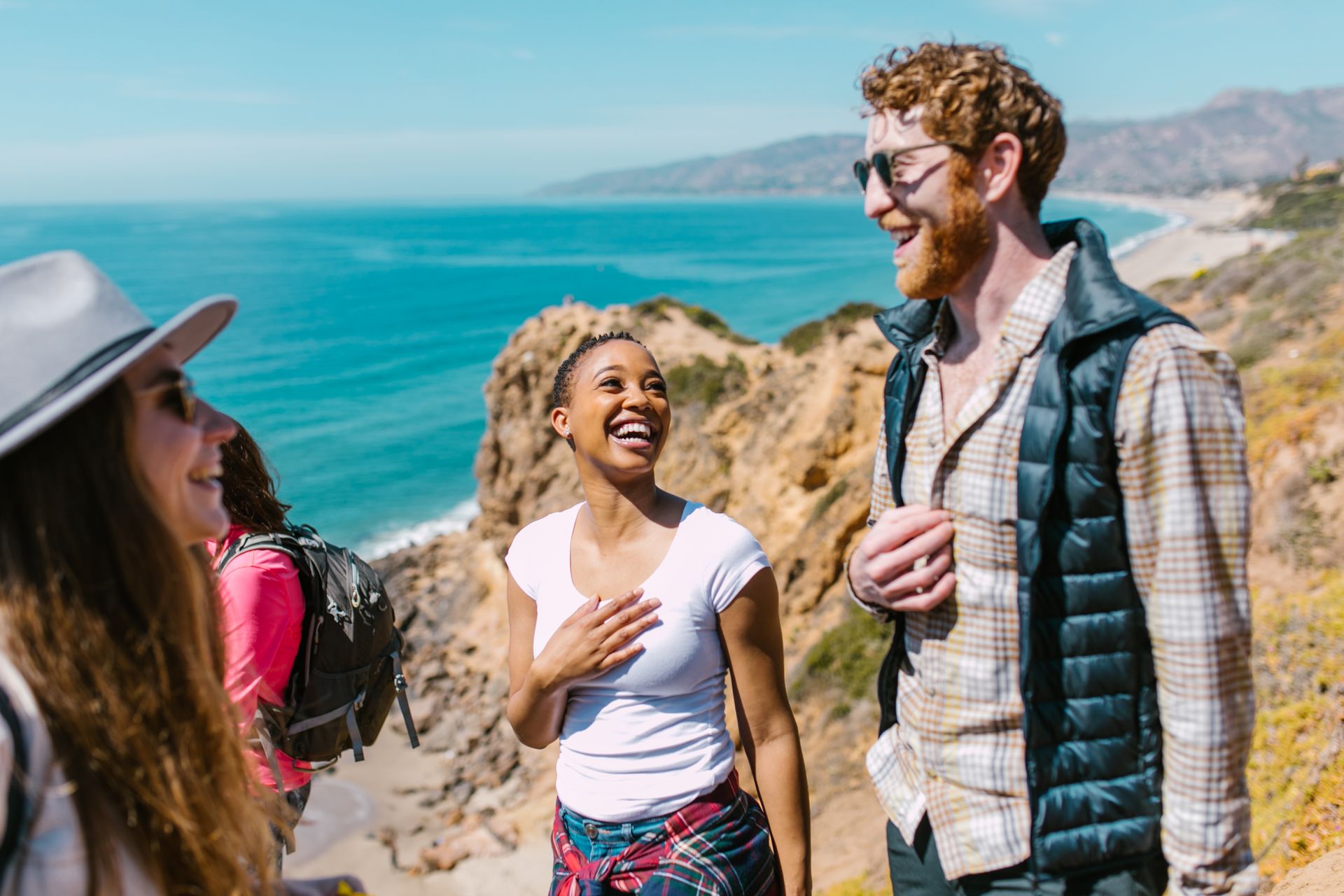 Joyful friends exploring a picturesque coastal trail under the sunny sky.