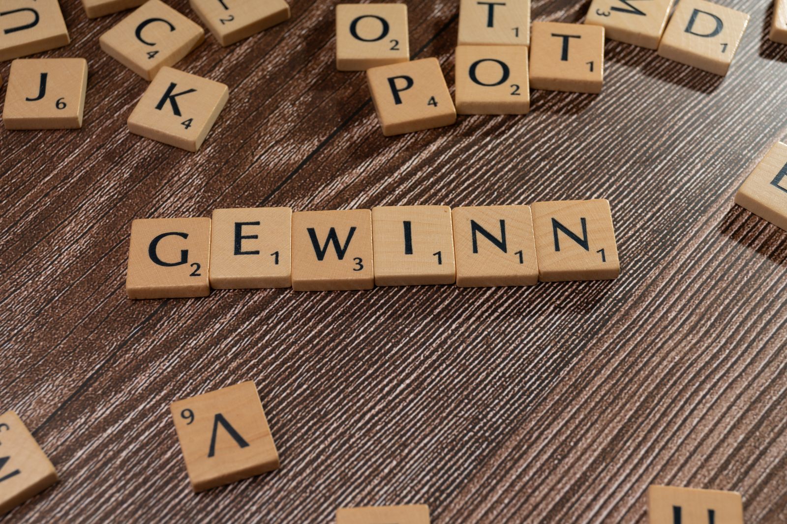 Scrabble tiles spelling the German word GEWINN on a wooden surface