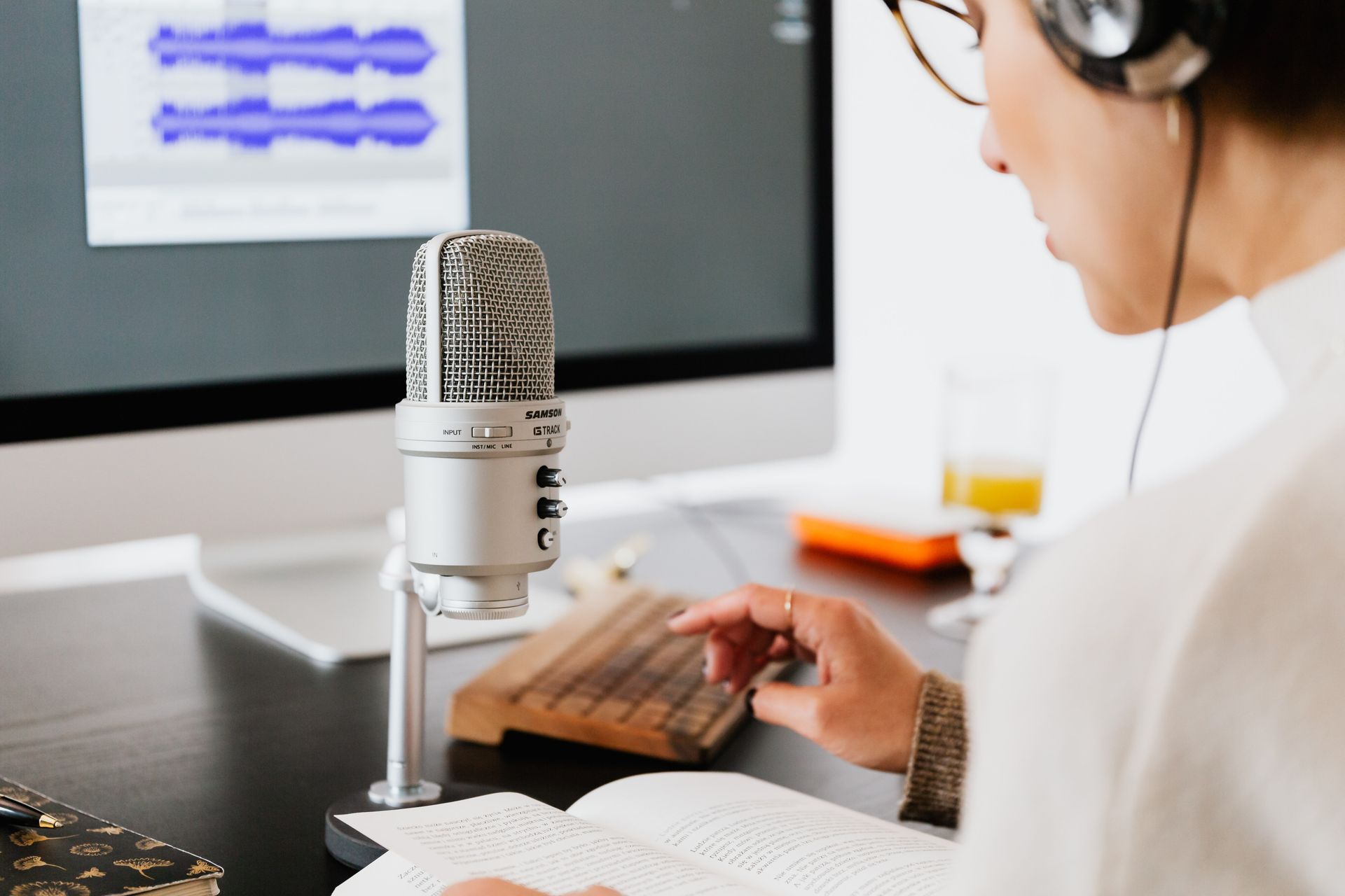 Person wearing headphones and reading from a book into a microphone
