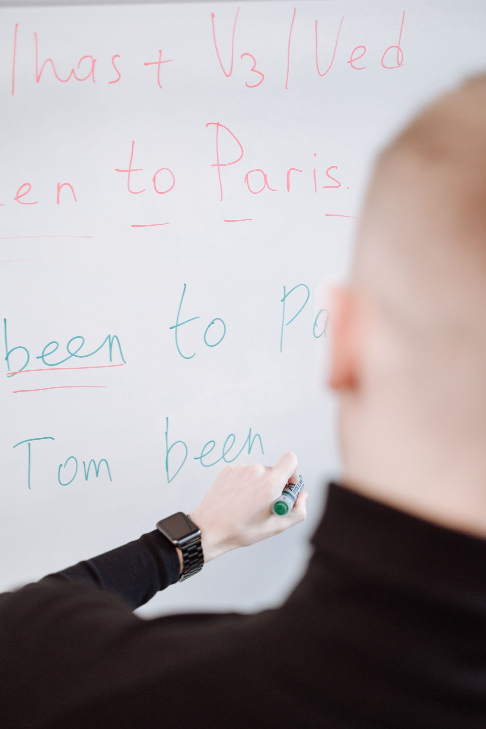 Person writing grammar explanations on a whiteboard with a marker