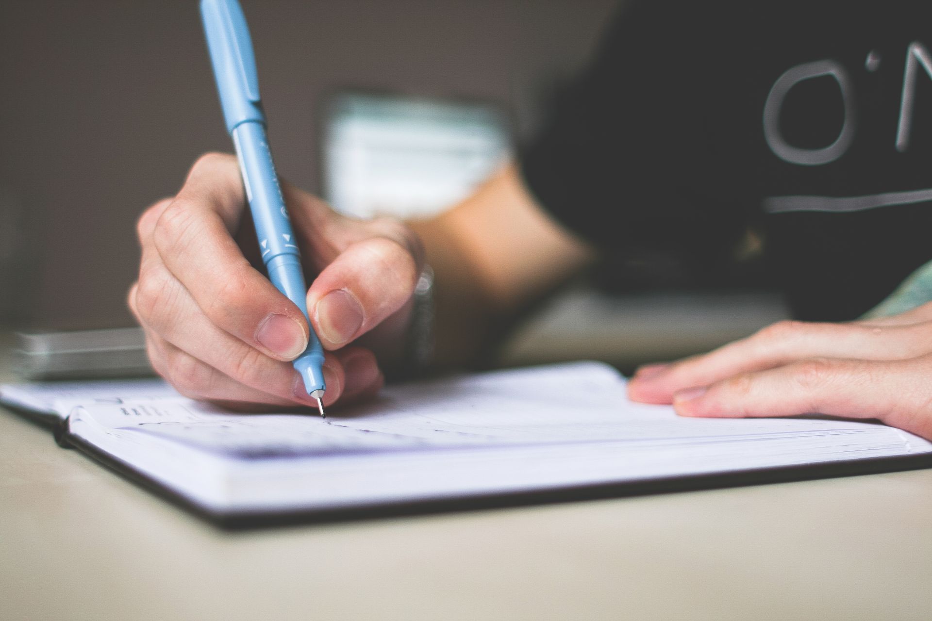 Close-up of a hand writing in a notebook with a blue pen