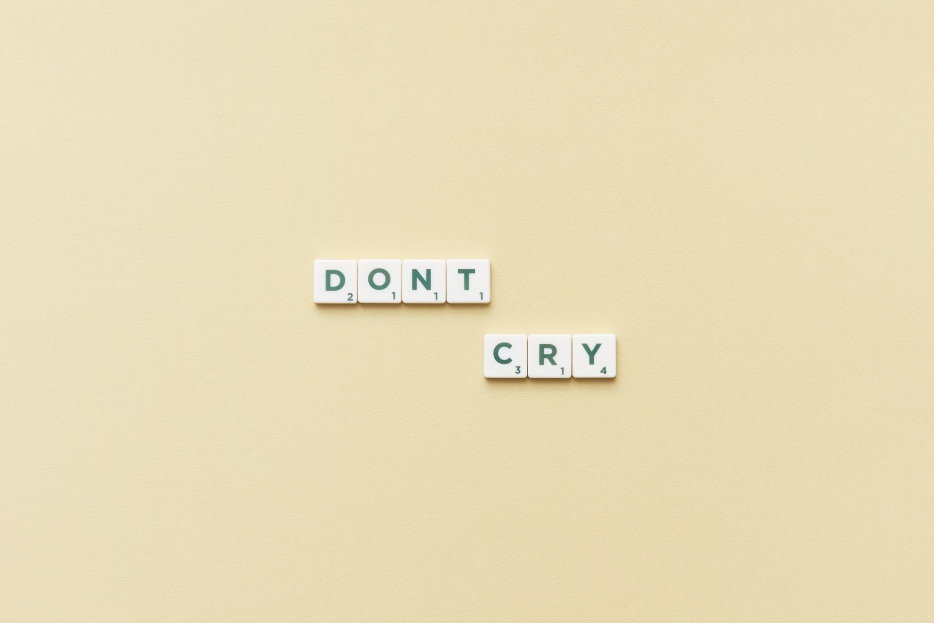 Scrabble tiles forming the phrase 'Don't Cry' on a simple yellow background, top view.