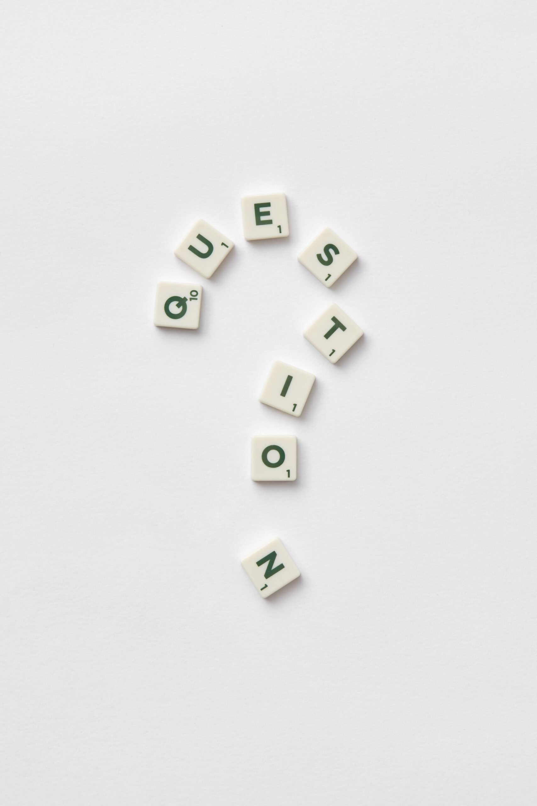 Artistic arrangement of letter tiles forming a question mark on a white background.