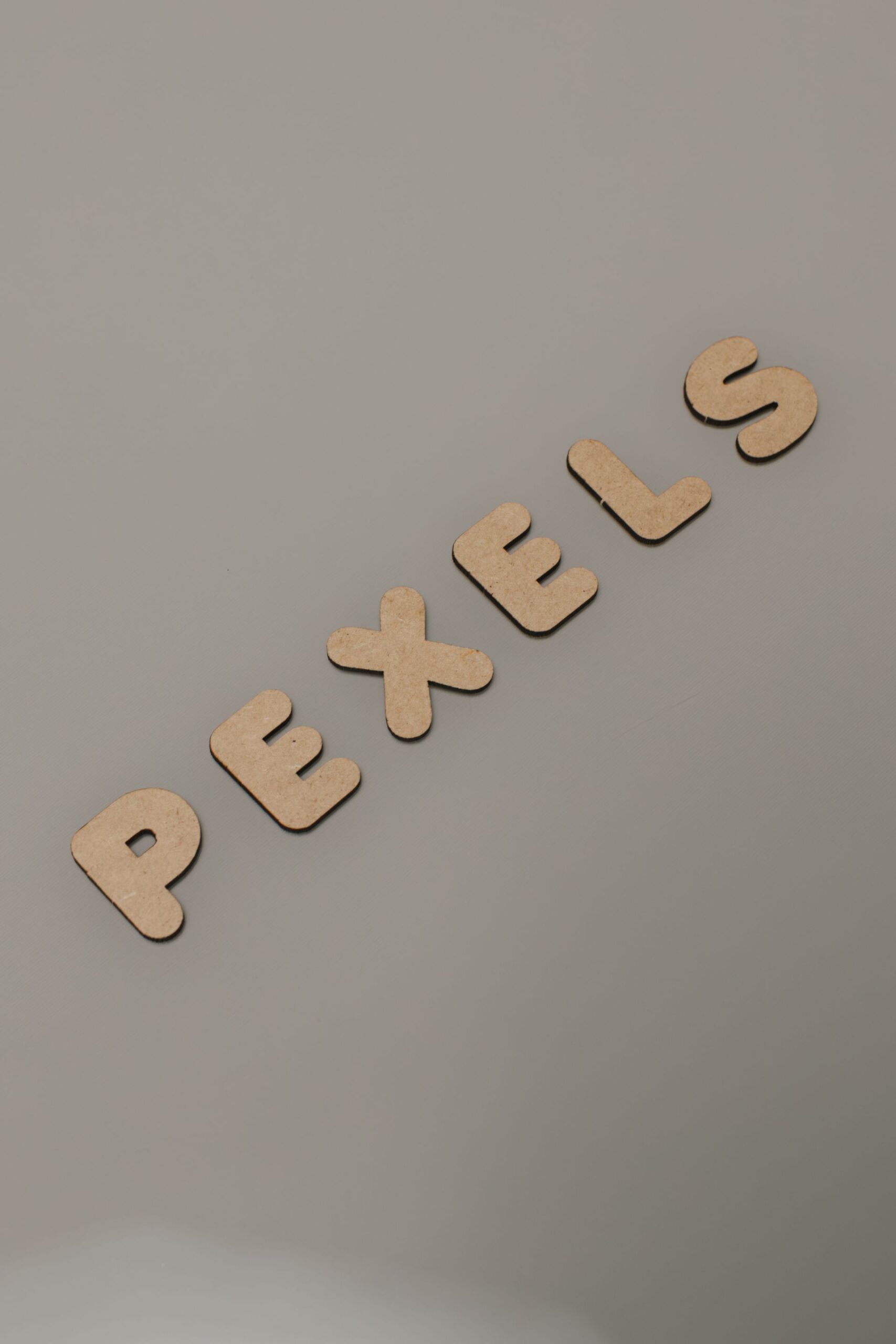 Wooden letters spelling "Pexels" on a minimalist gray background for creative design uses.