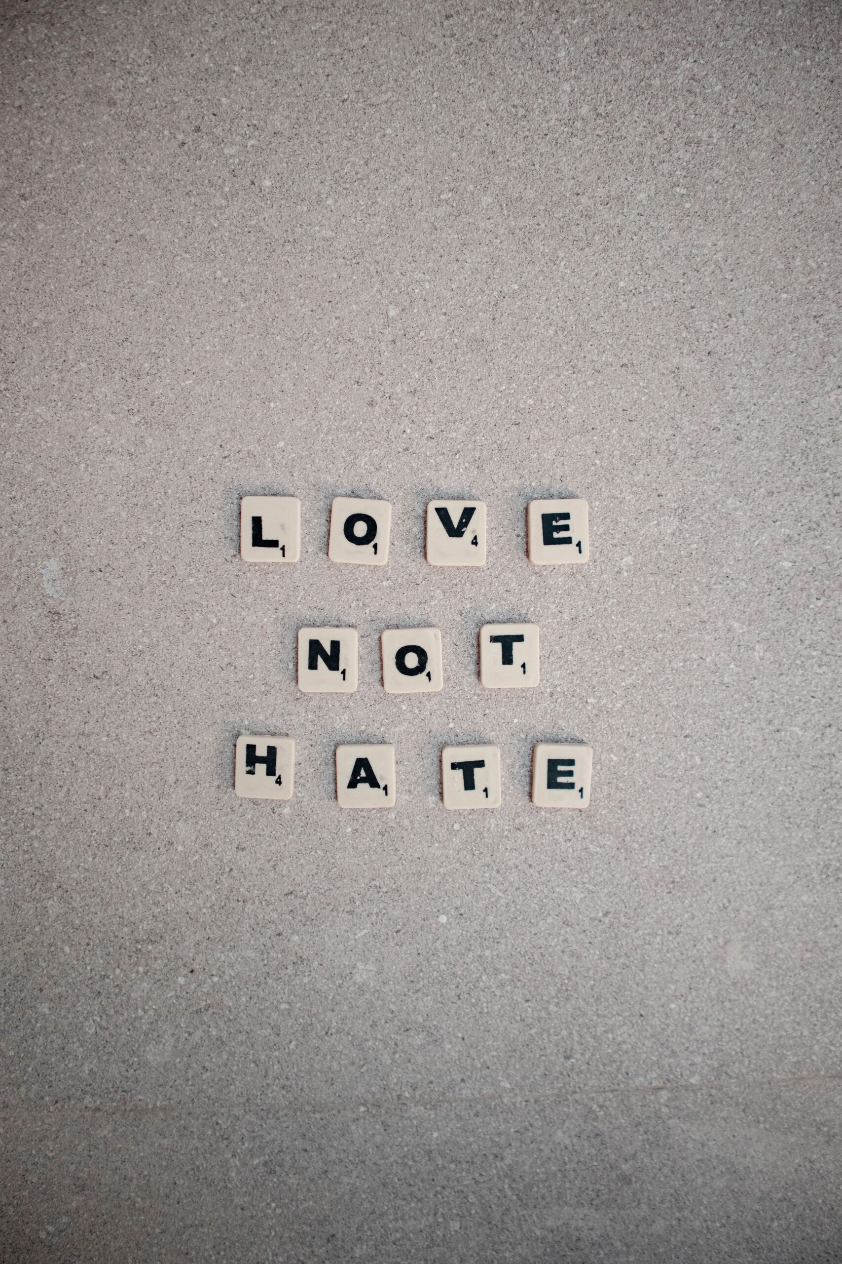 Scrabble tiles forming the words 'Love Not Hate' on a concrete background, promoting positivity.