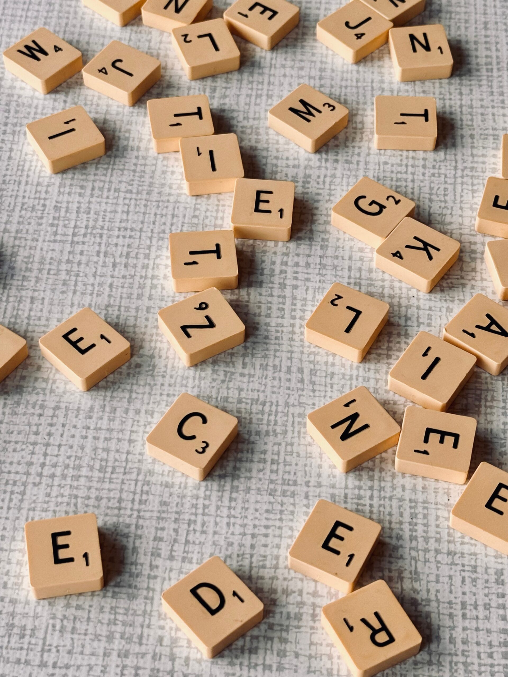 A collection of Scrabble tiles scattered across a textured surface, showcasing letters and point values.