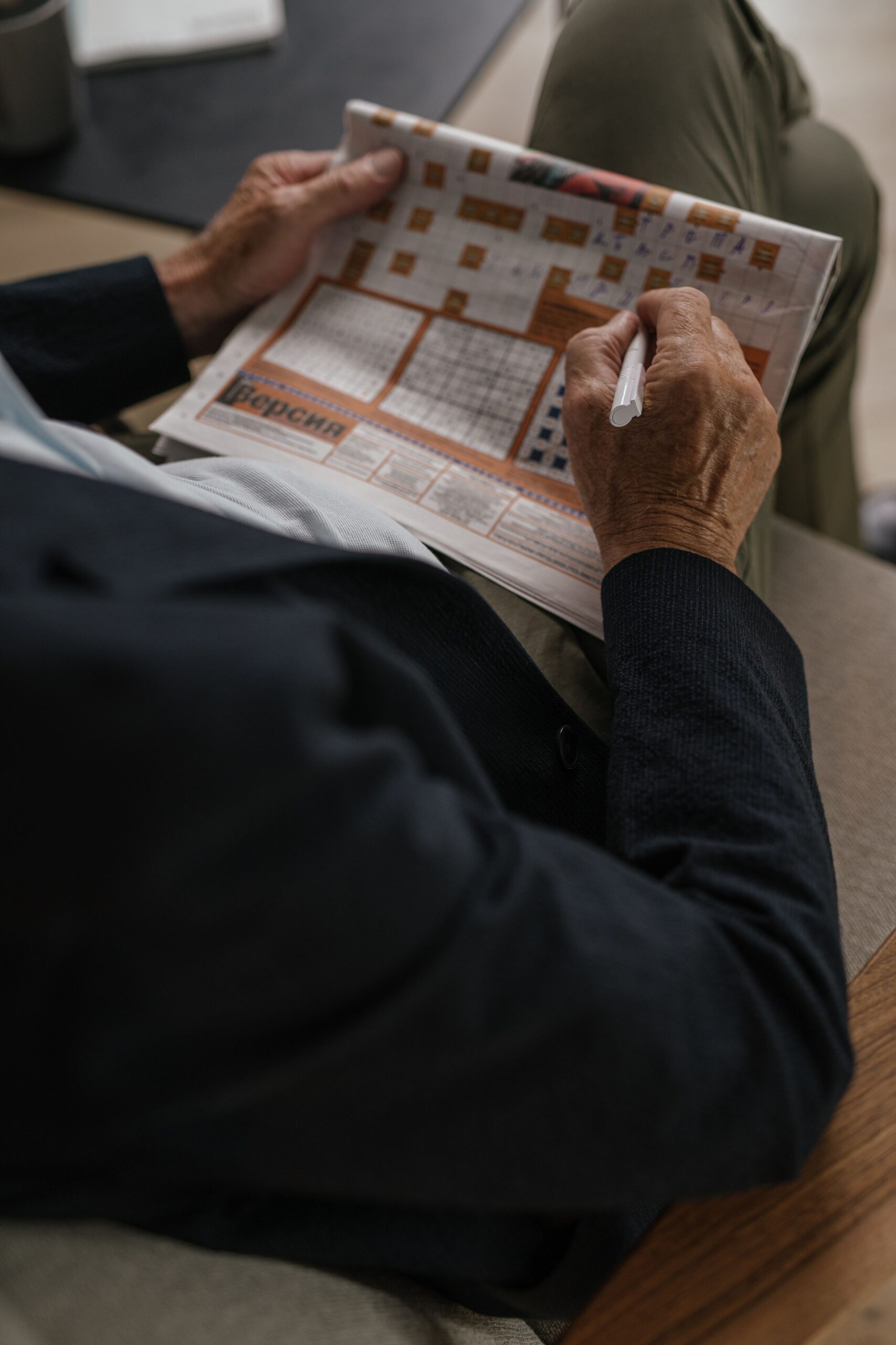 Senior adult solving a crossword puzzle in a newspaper, captured indoors.