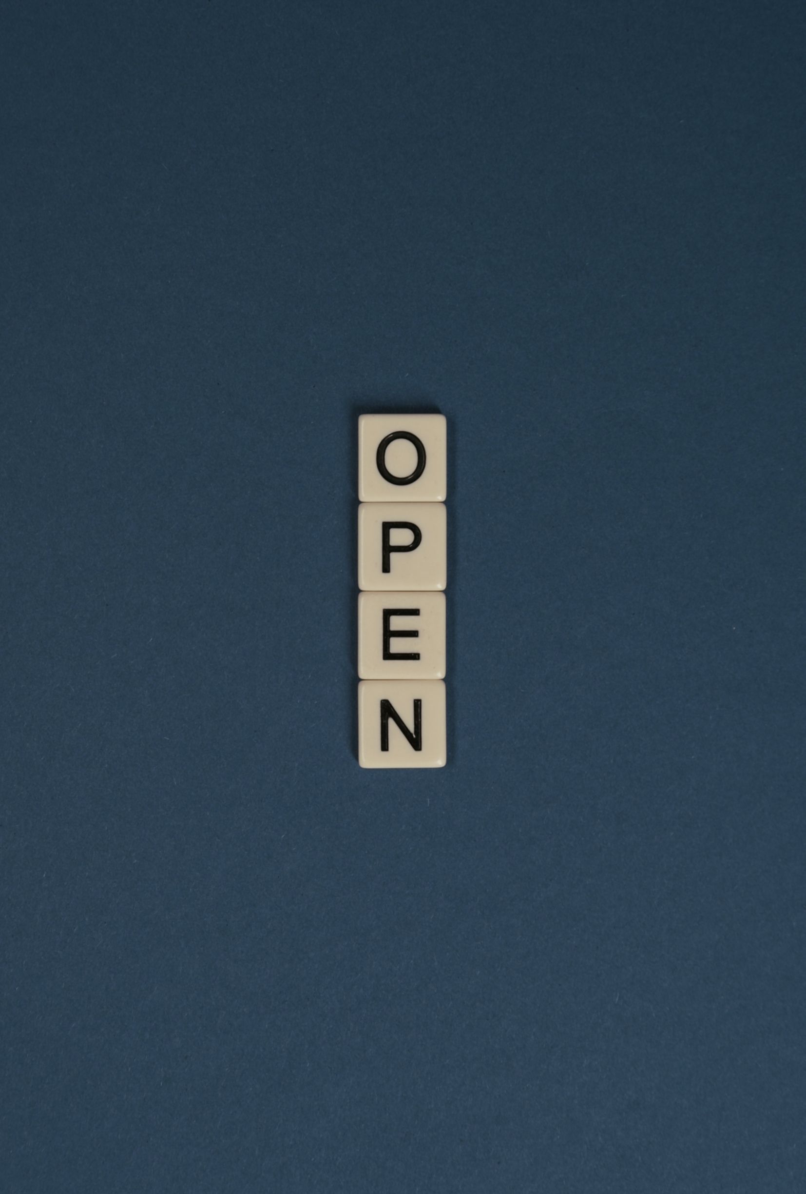 Scrabble tiles spelling 'OPEN' vertically on a blue background, ideal for copyspace.