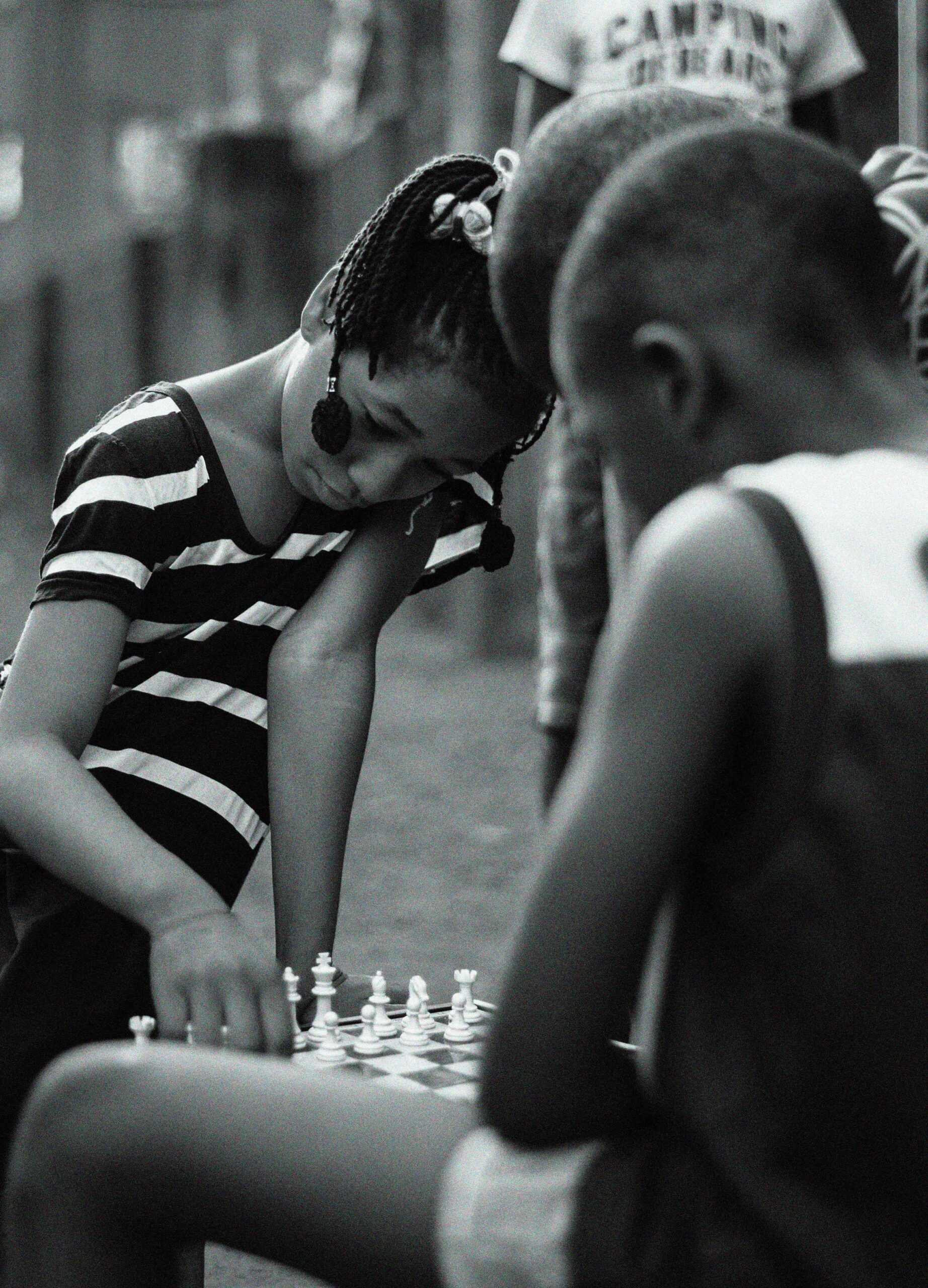 Young children engaged in a game of chess outside, captured in classic black and white.