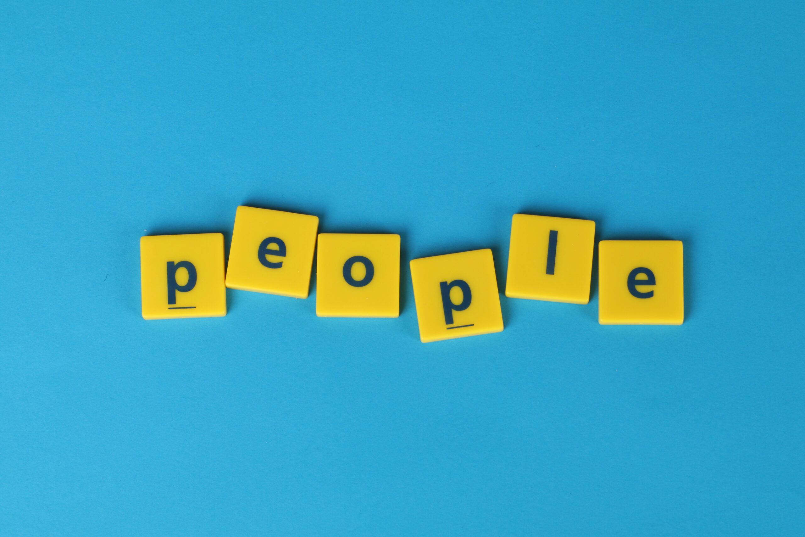 Yellow Scrabble tiles spelling 'people' on a blue background, vibrant and playful.