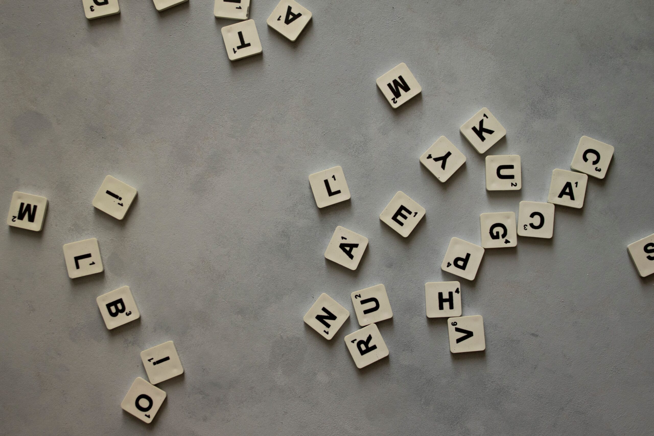 A collection of mixed letter tiles scattered across a textured grey surface.