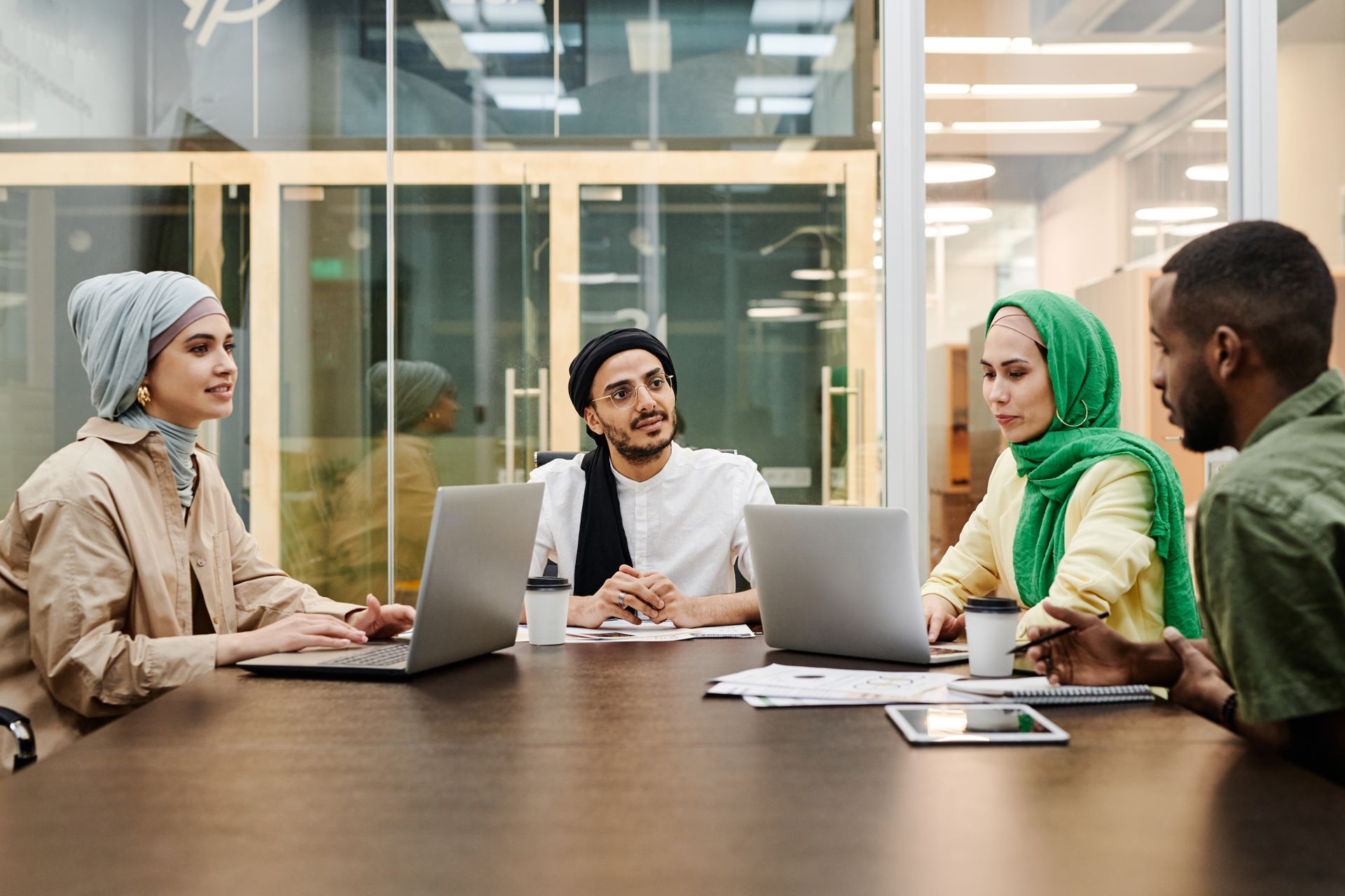 A diverse group discussing ideas in a modern office setting, using laptops and tablets