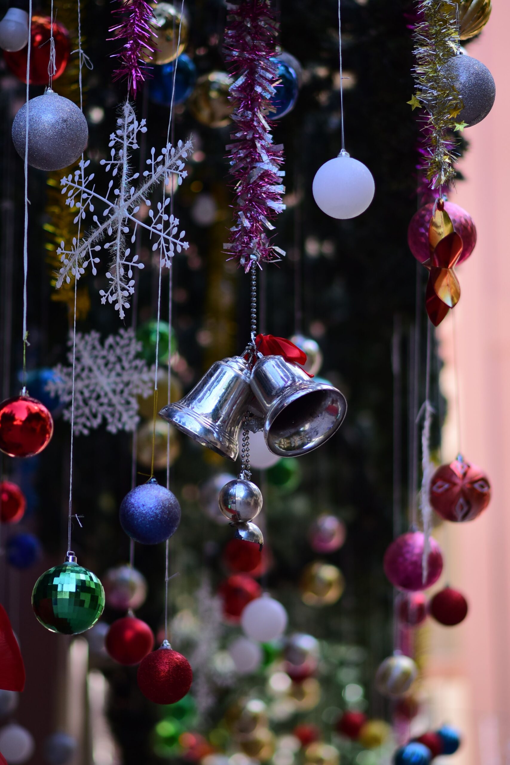 Colorful Christmas ornaments hanging from a festive display, featuring bells, baubles, and snowflakes.