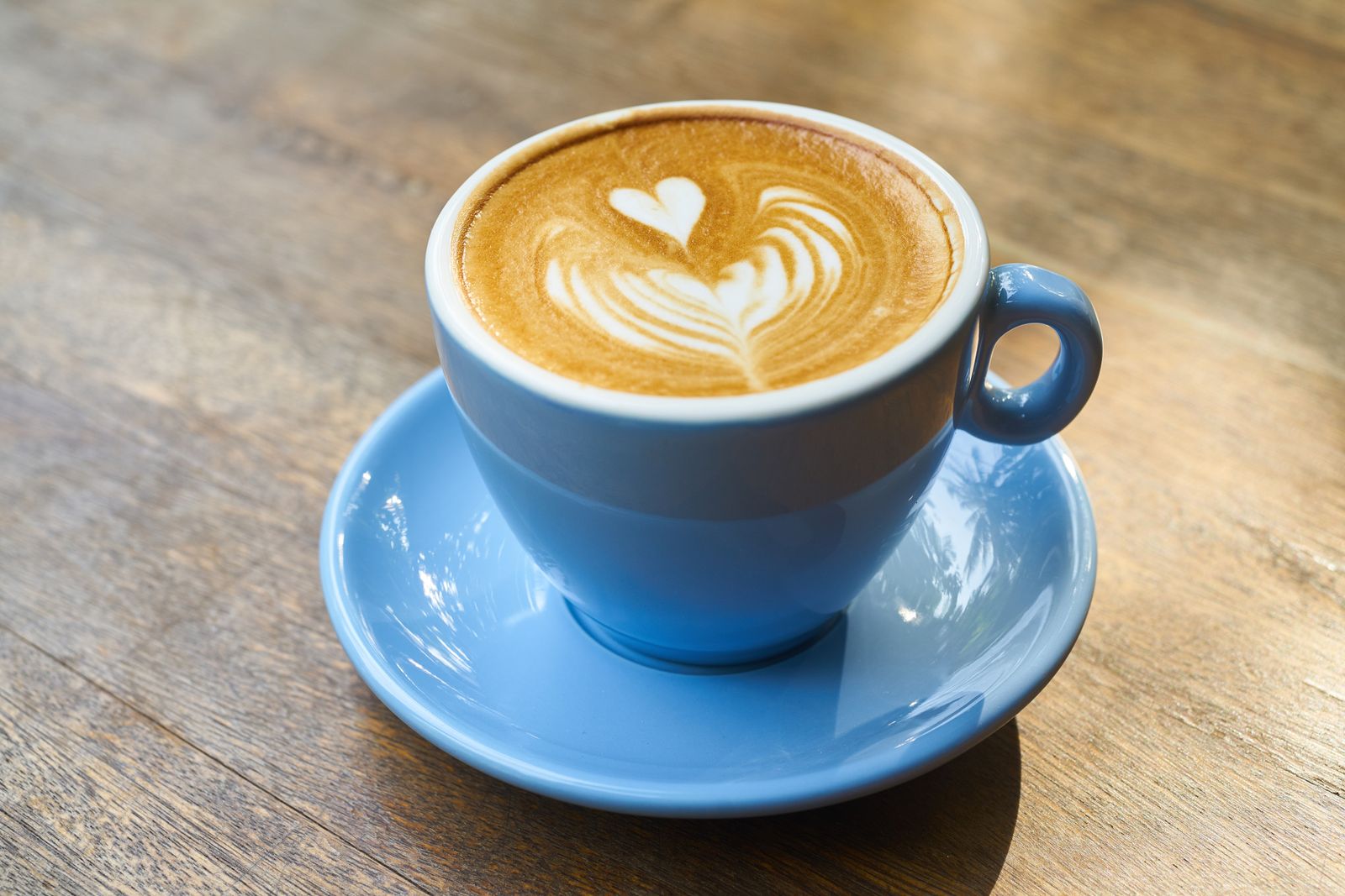 Cappuccino with heart-shaped latte art in a blue cup on a wooden table