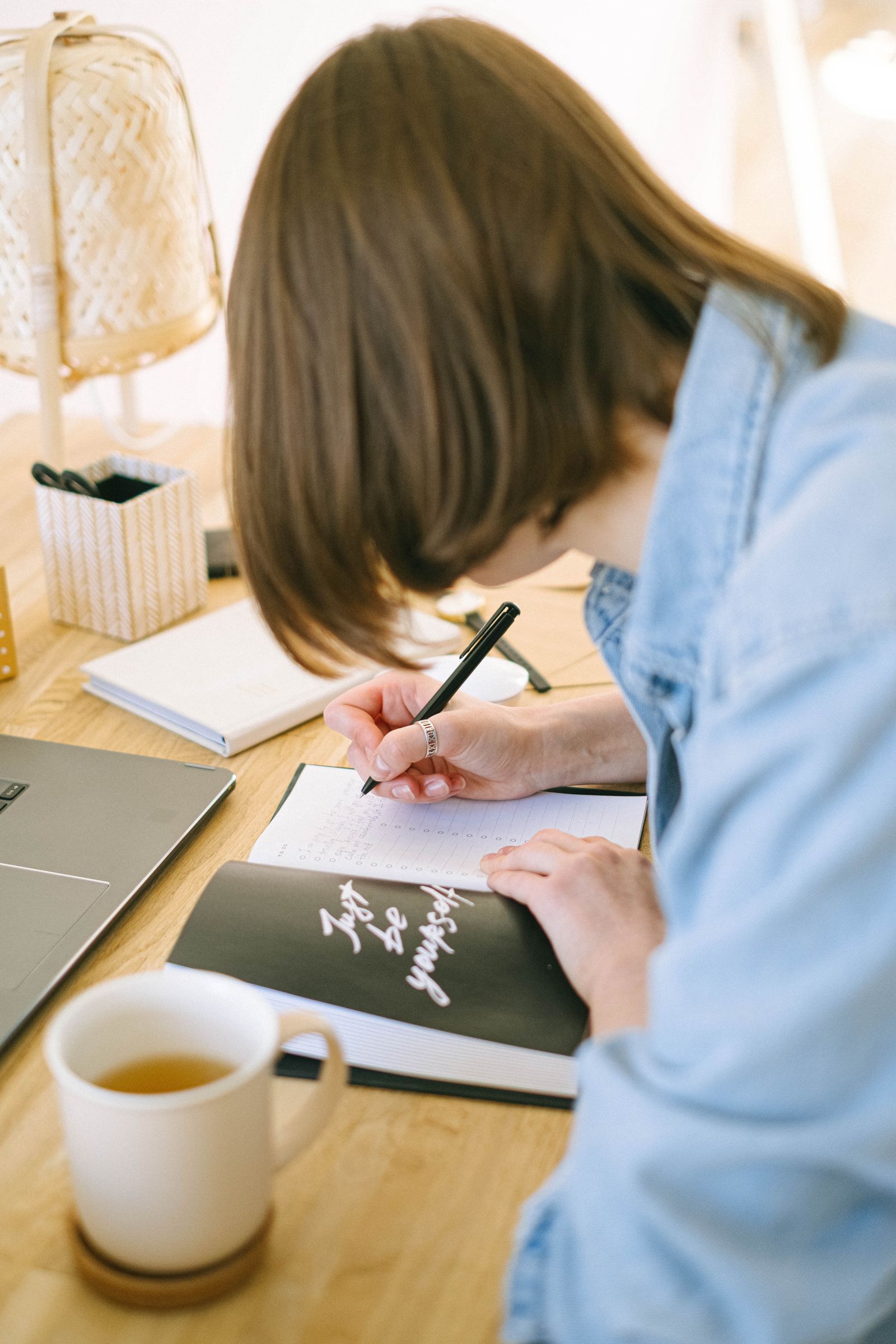 Adult woman writing with a pen in a notebook at a home office desk