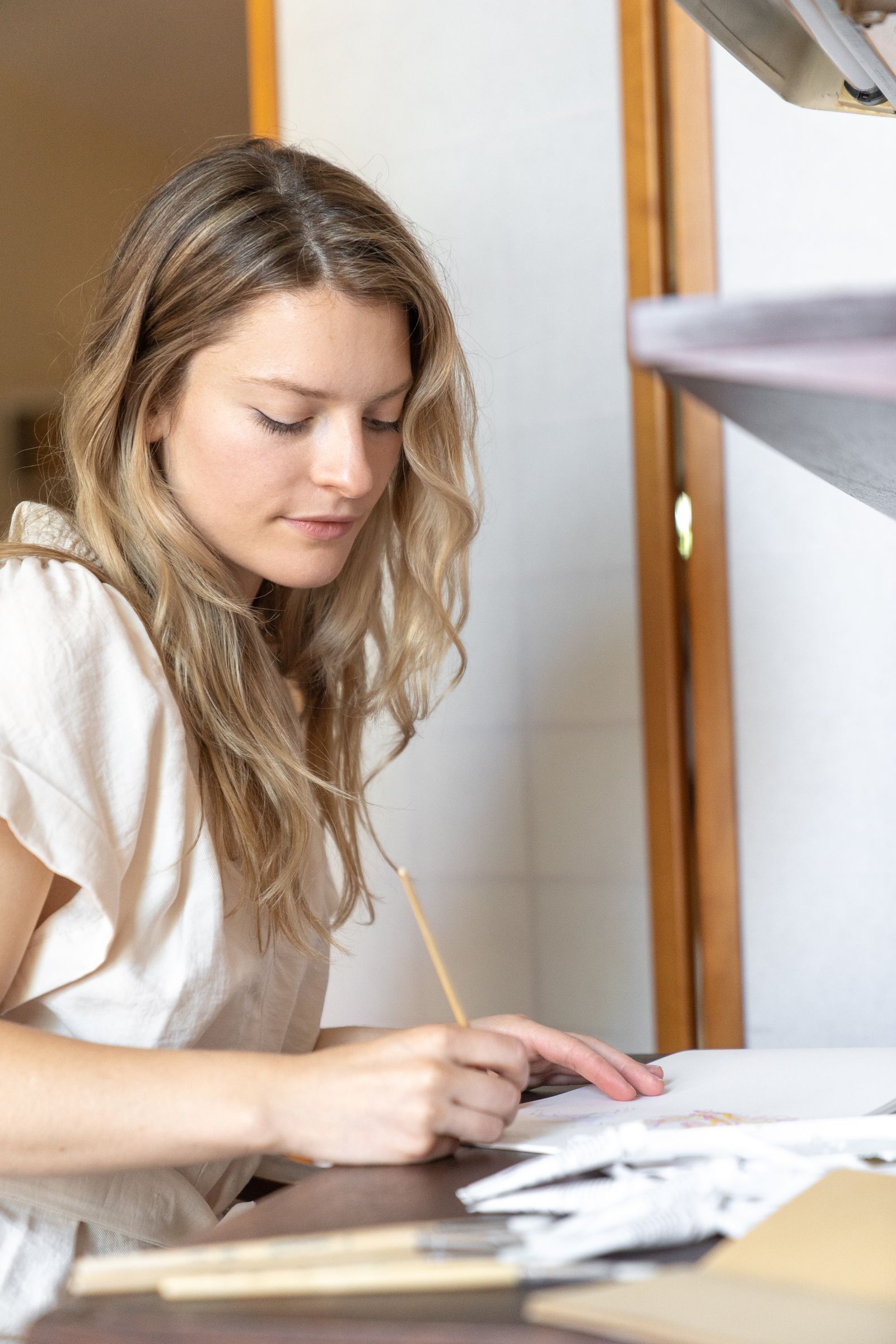 Young adult woman focused on writing in a notebook at a desk in a brightly lit indoor setting