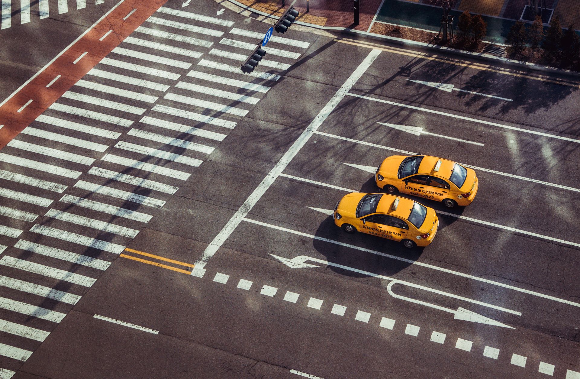 Two yellow taxis navigate a city intersection with marked pedestrian crossings.