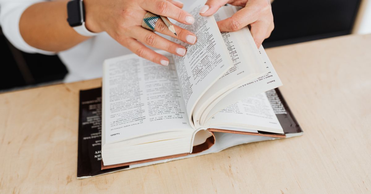 Woman turning the pages of a dictionary on a wooden desk