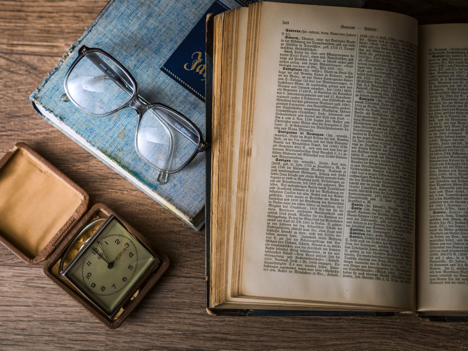 Open book beside sunglasses and a clock on a table