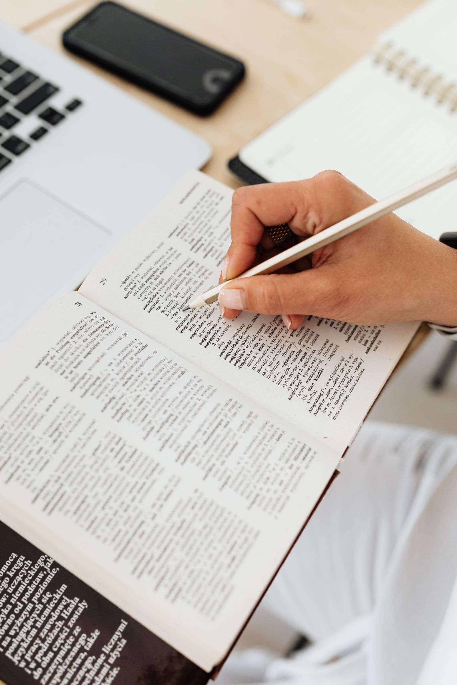 Woman underlining words in a book at a desk with a laptop