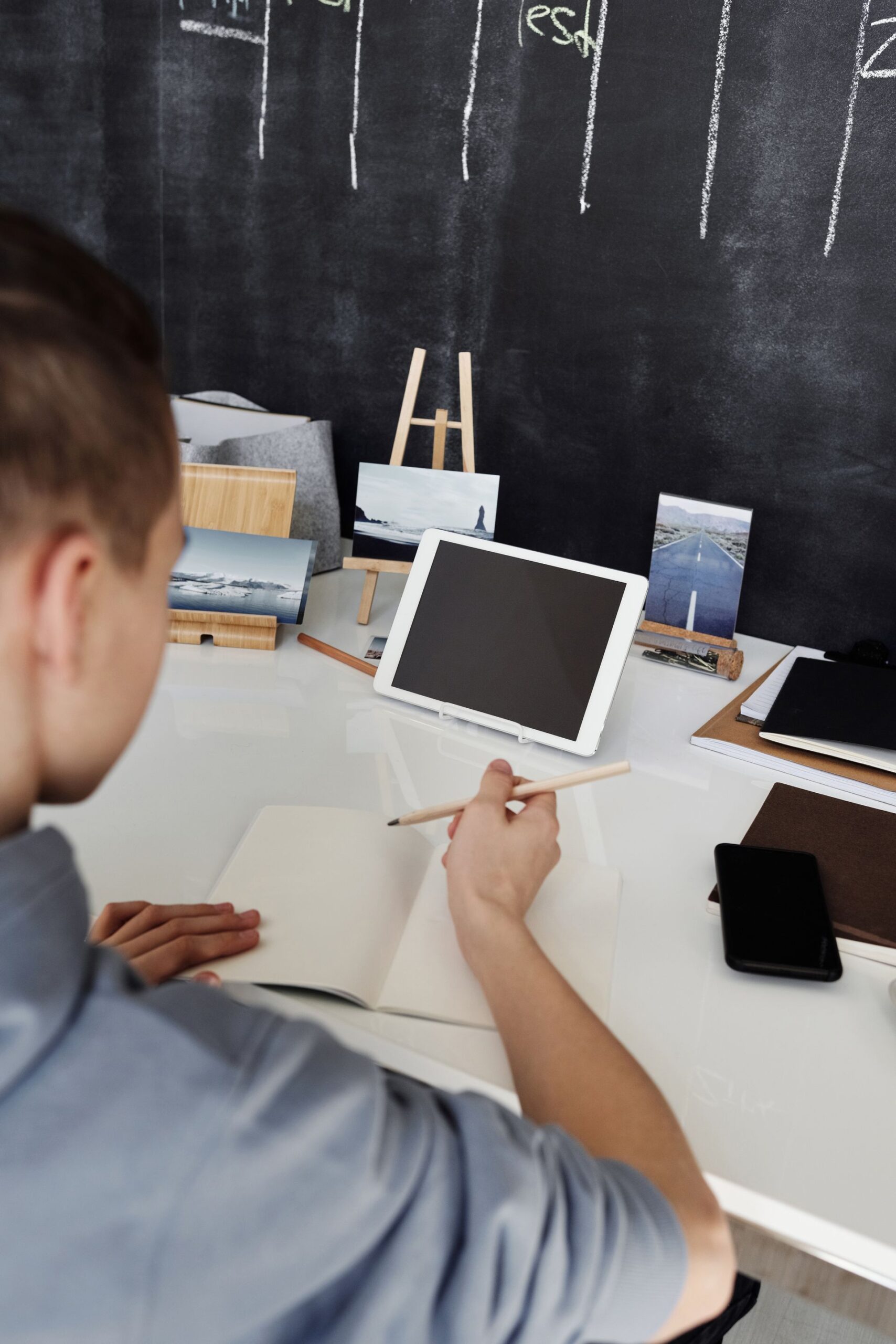 Teenager studying with tablet and notebook at a white desk