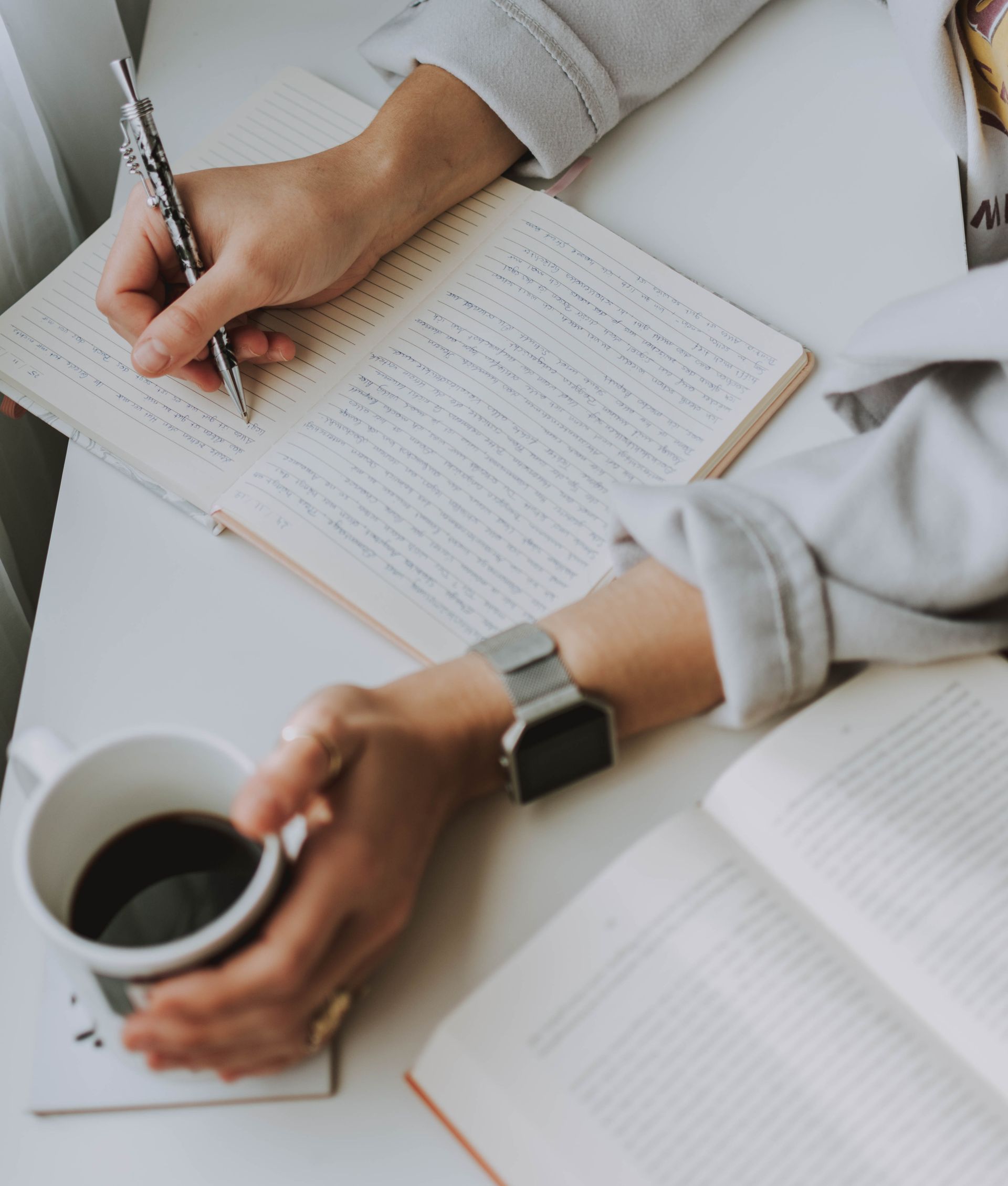 Close-up of a person writing in a notebook with coffee