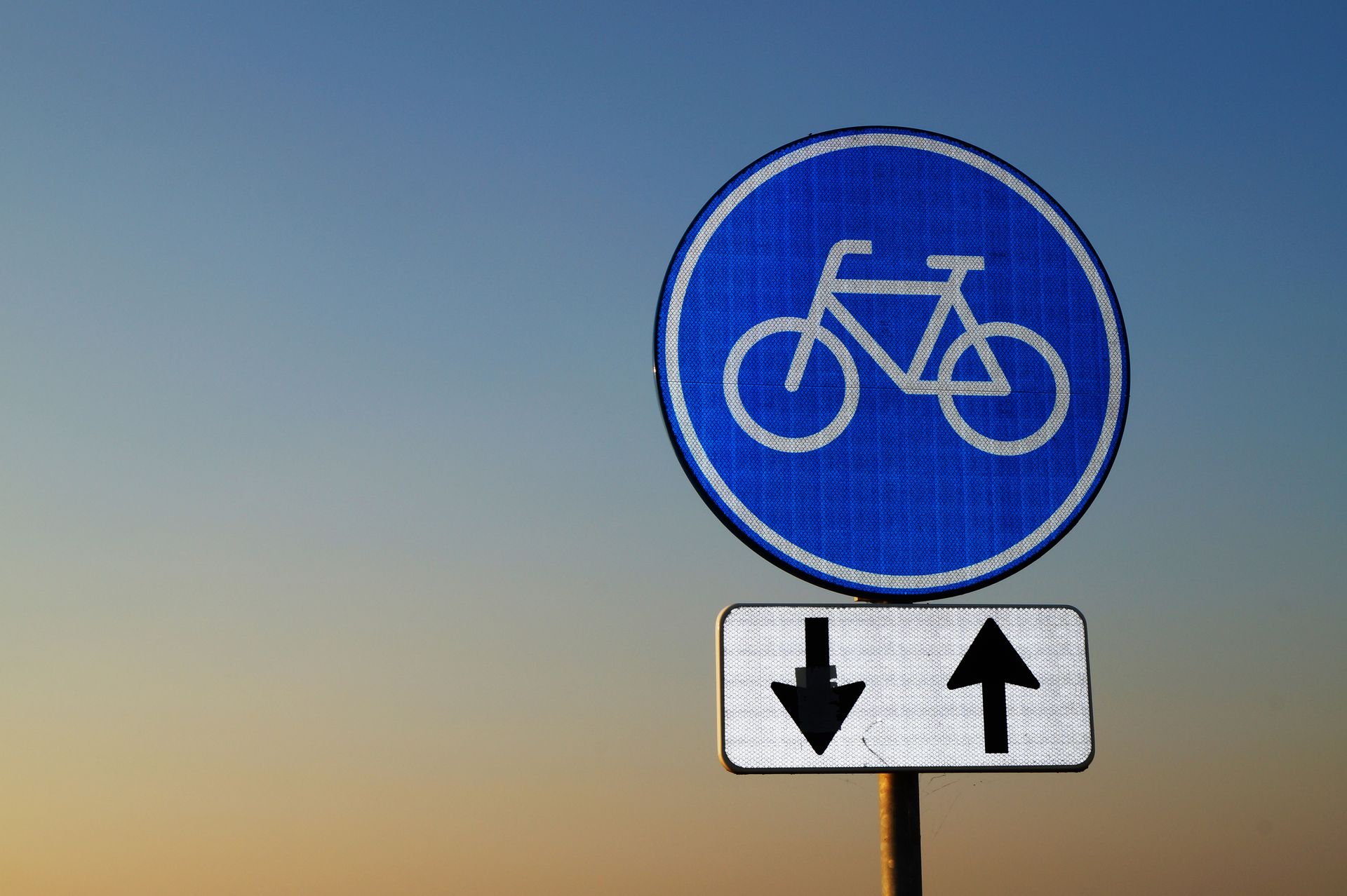 Bicycle route sign with directional arrows against twilight sky
