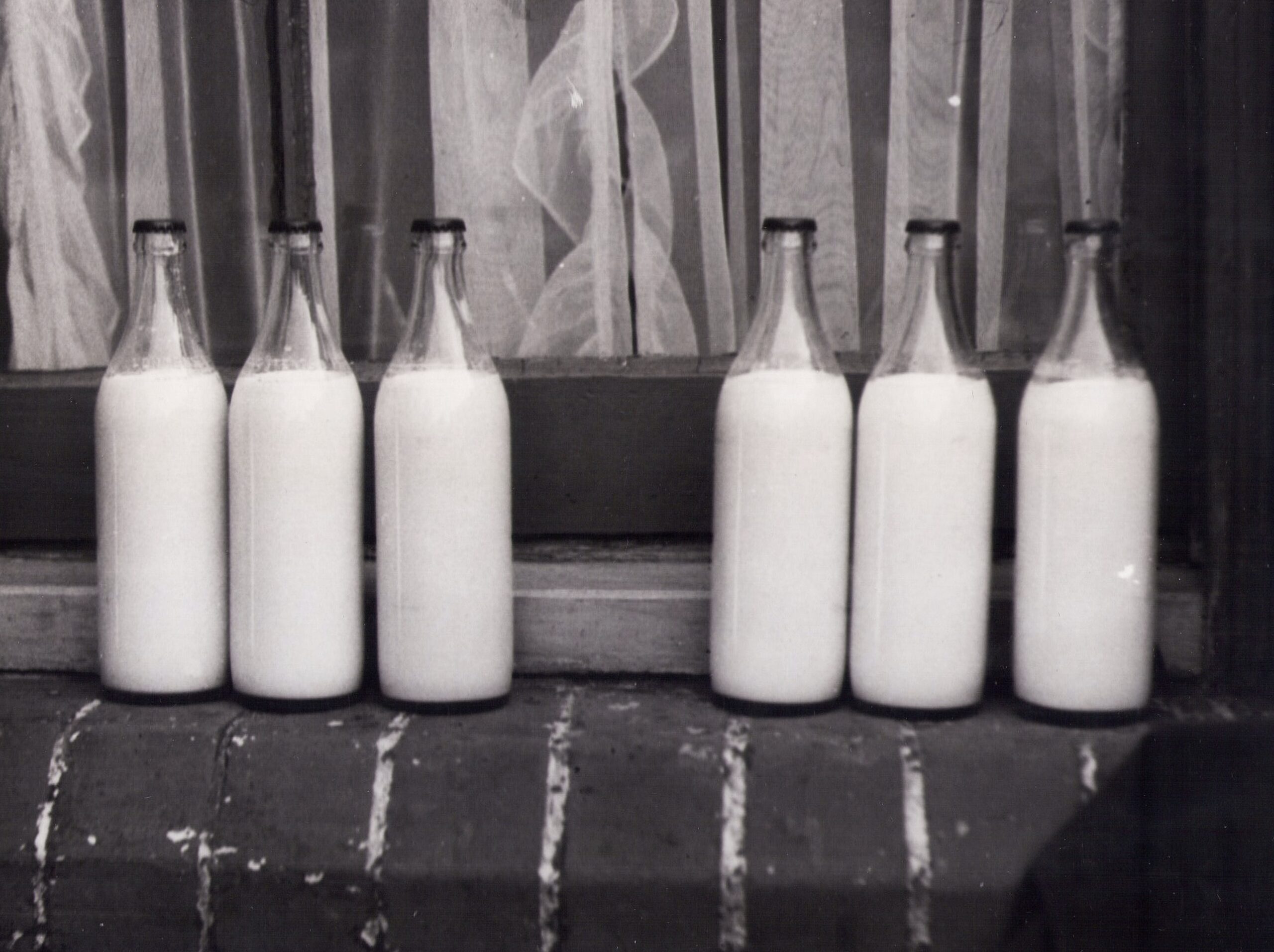 Vintage photo of glass milk bottles on a brick windowsill in monochrome.