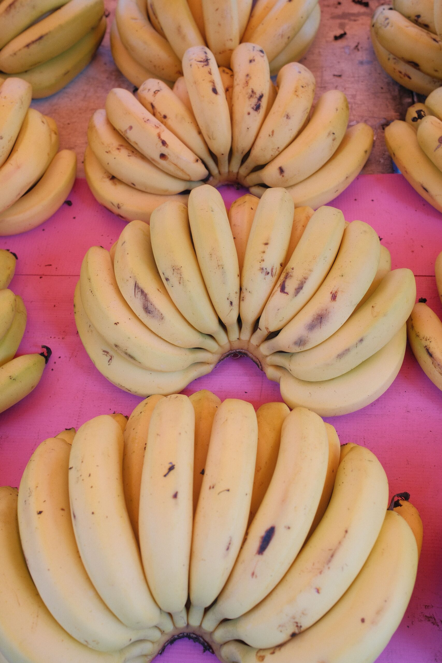 Vibrant display of ripe bananas against a pink backdrop at a market.